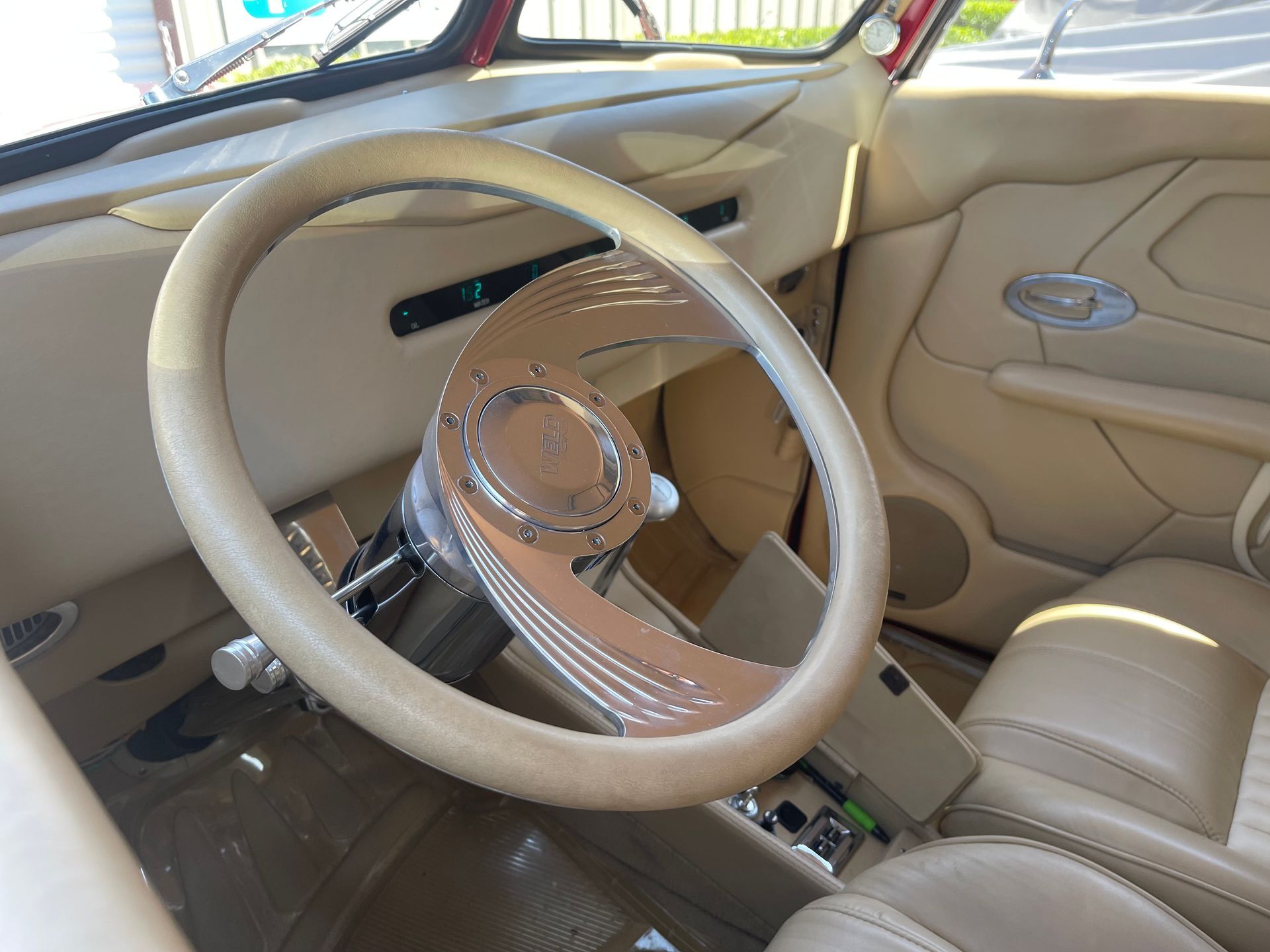 The tan interior of a classic car, featuring a custom steering wheel and a clean, minimalist dashboard.