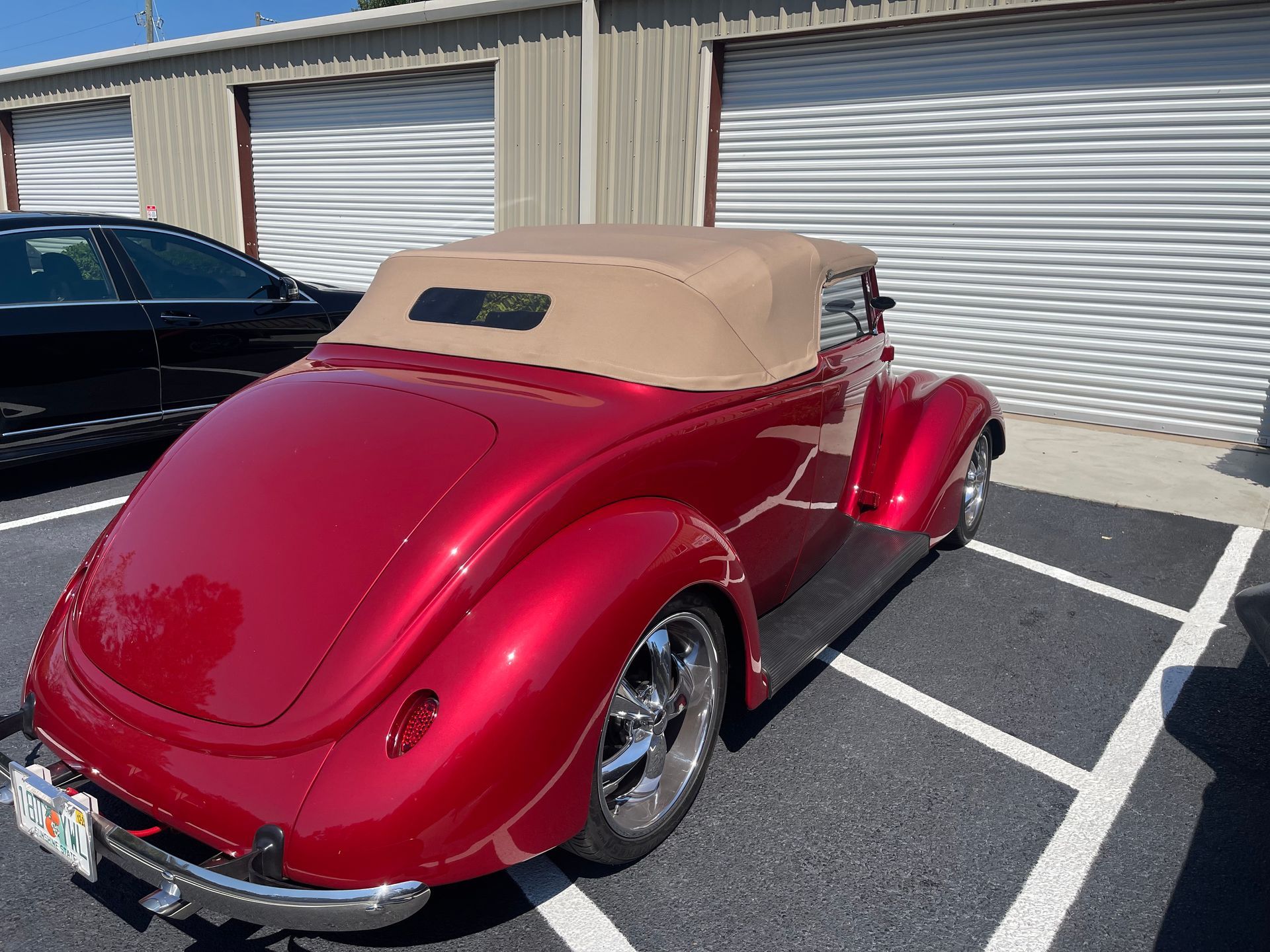 A shiny red vintage convertible with a tan soft top parked in a parking lot.
