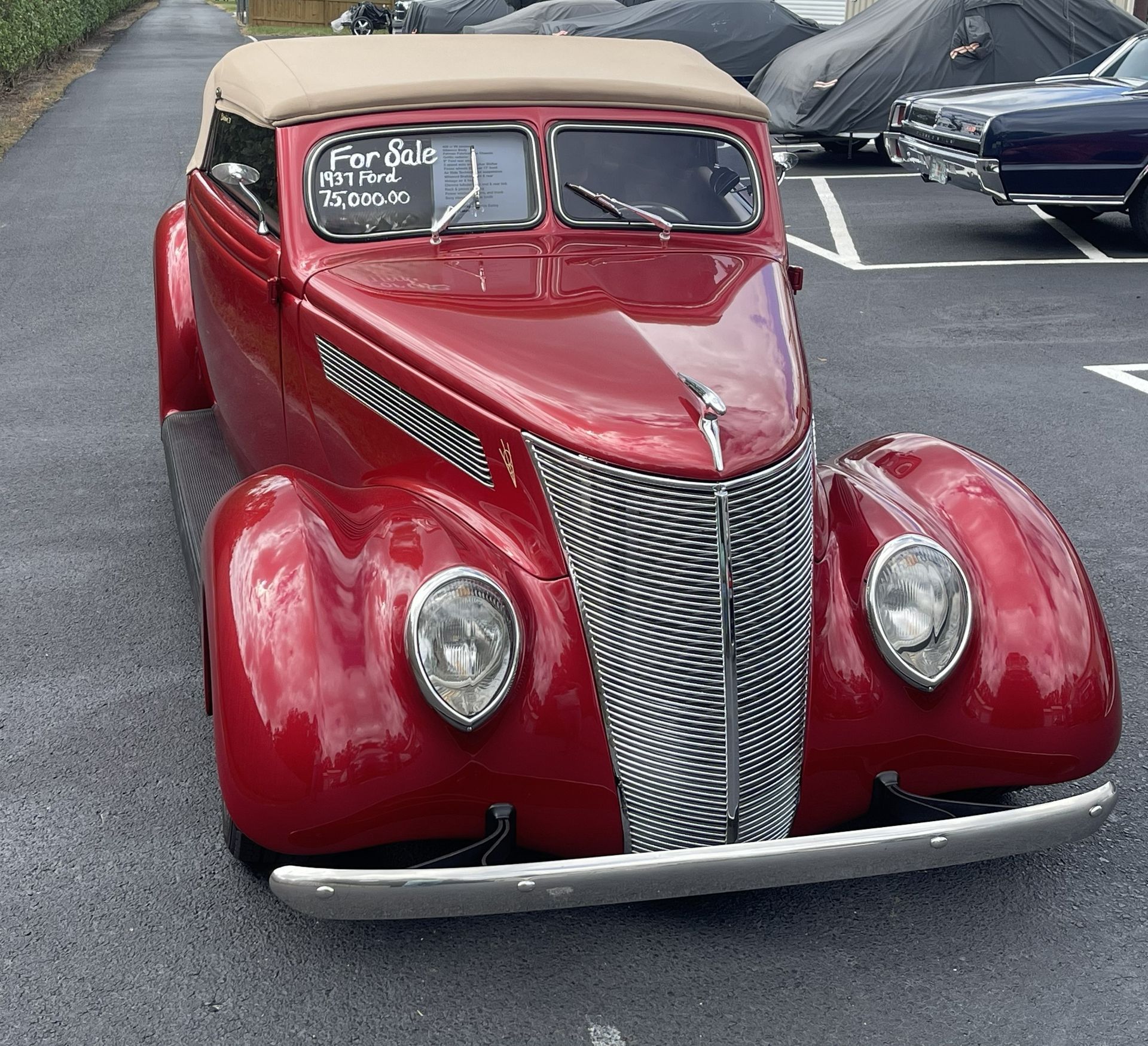 A classic red 1937 Ford convertible with a tan top parked in a lot, displaying a