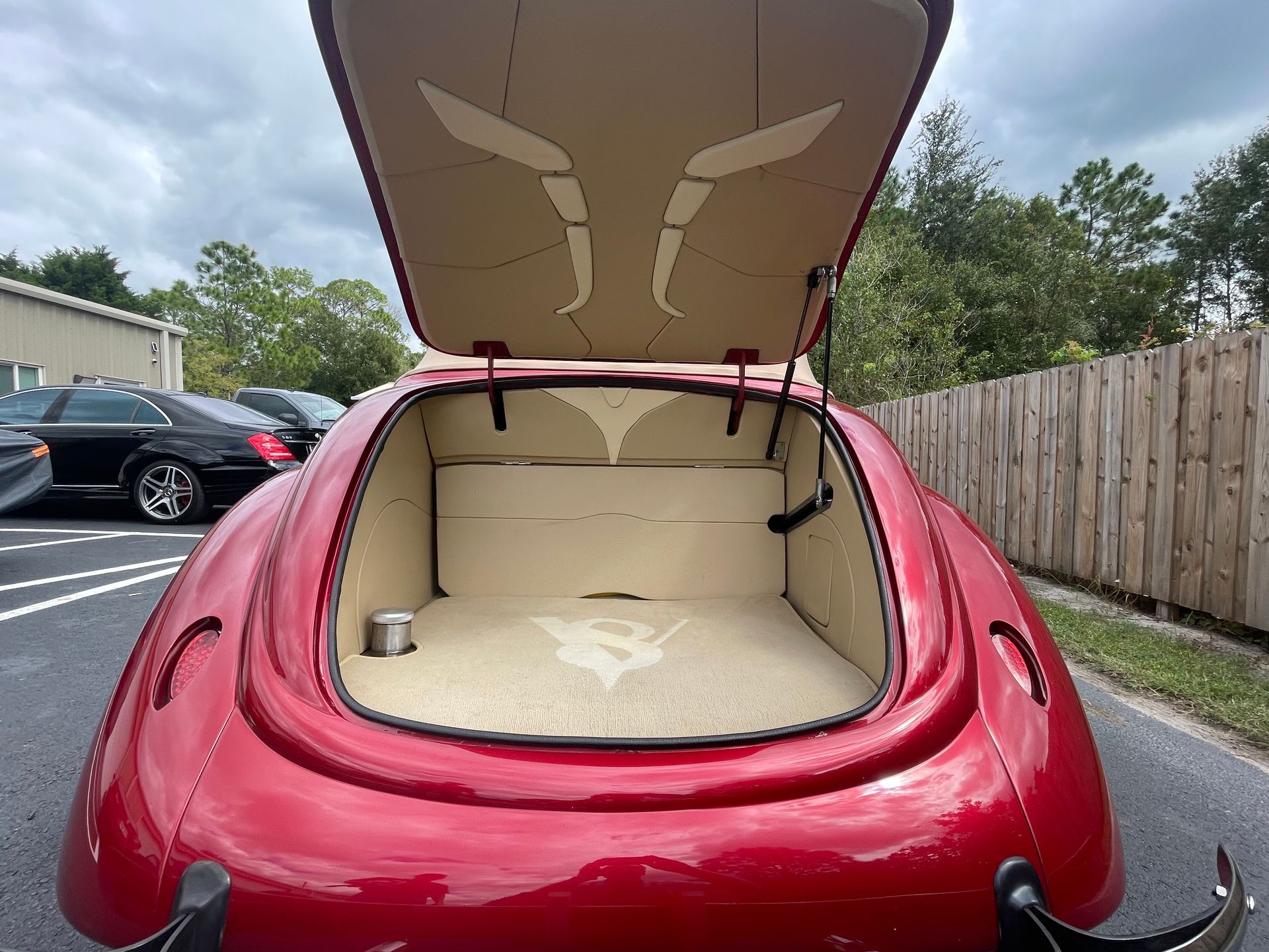 A rear view of a cherry-red custom car with its trunk open, revealing a tan, minimalist interior design.