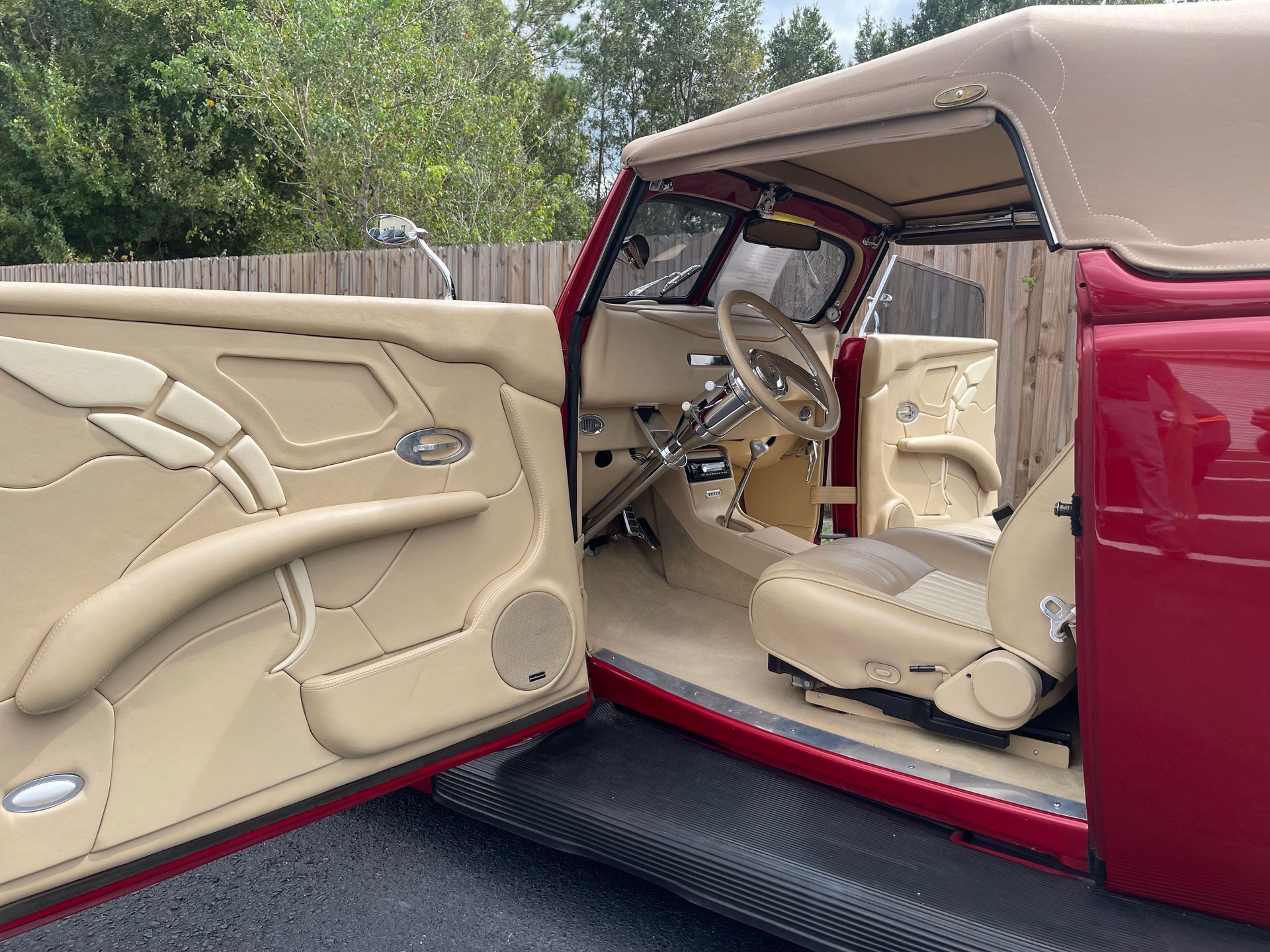Interior view of a classic red convertible with custom cream-colored leather upholstery, visible dashboard, and open door.