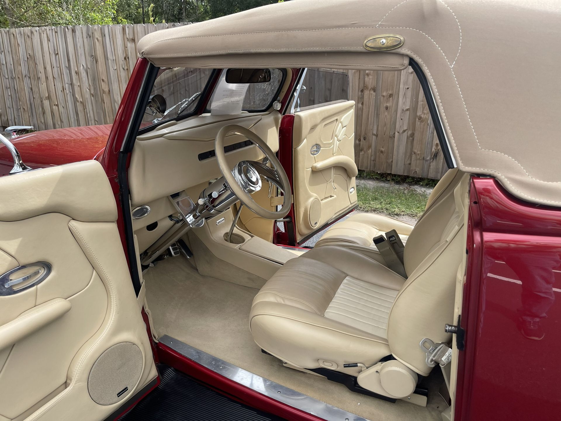 The interior of a classic red convertible with beige leather upholstery, bucket seats, and a tan fabric roof.