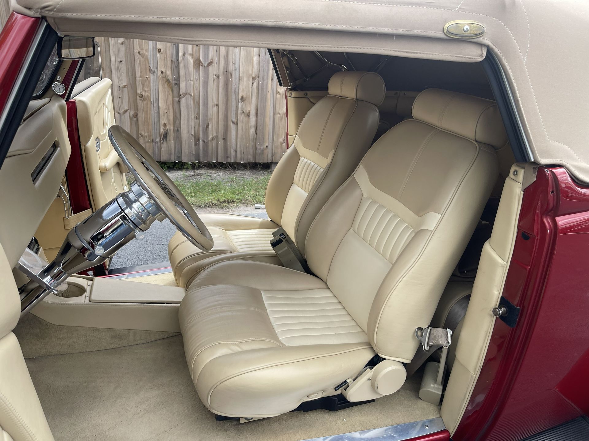 The interior of a classic convertible with tan leather bucket seats, a chrome steering wheel, and red door panels.