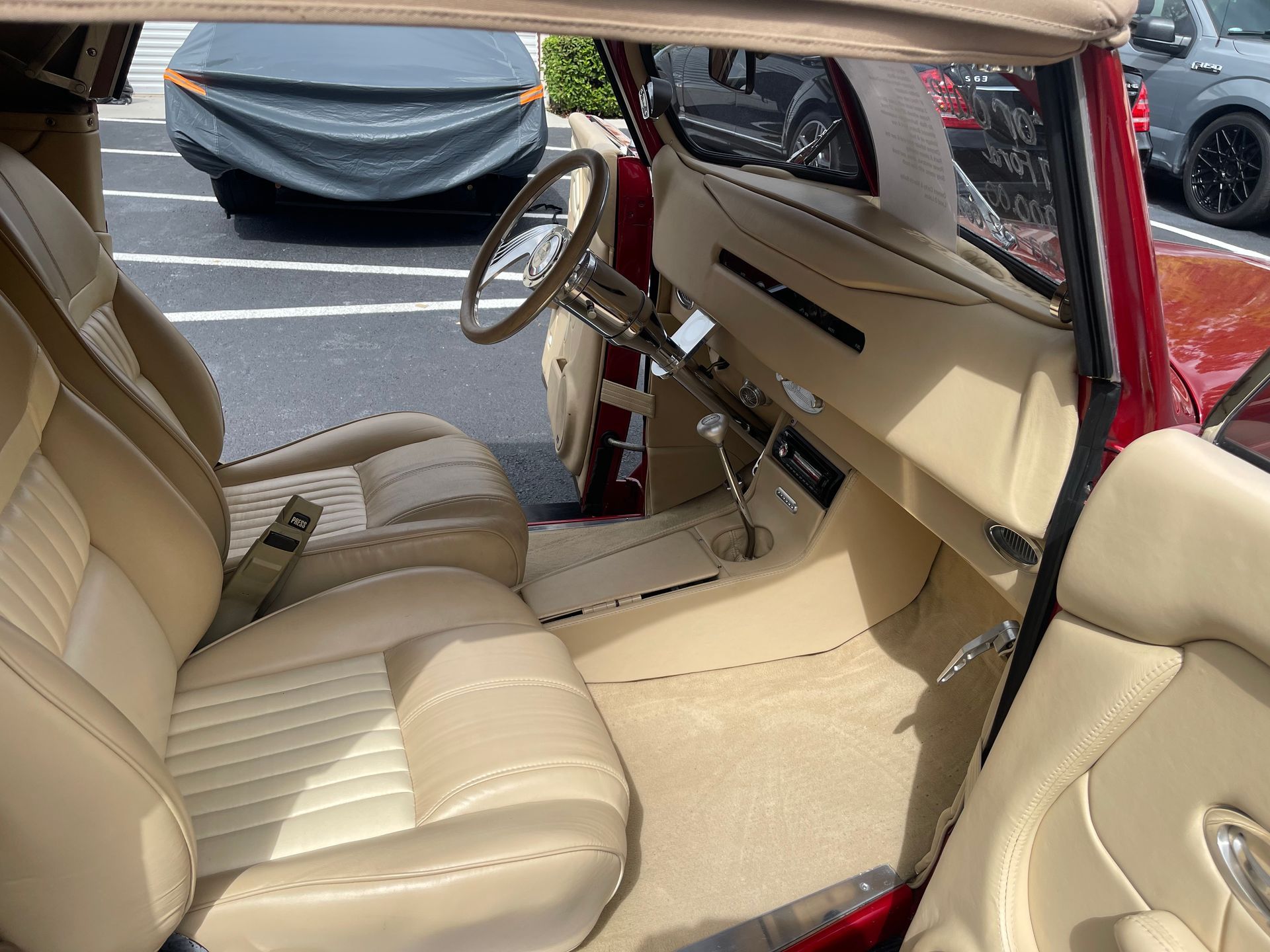 The interior of a classic red convertible car, featuring beige leather bucket seats and a matching dashboard.