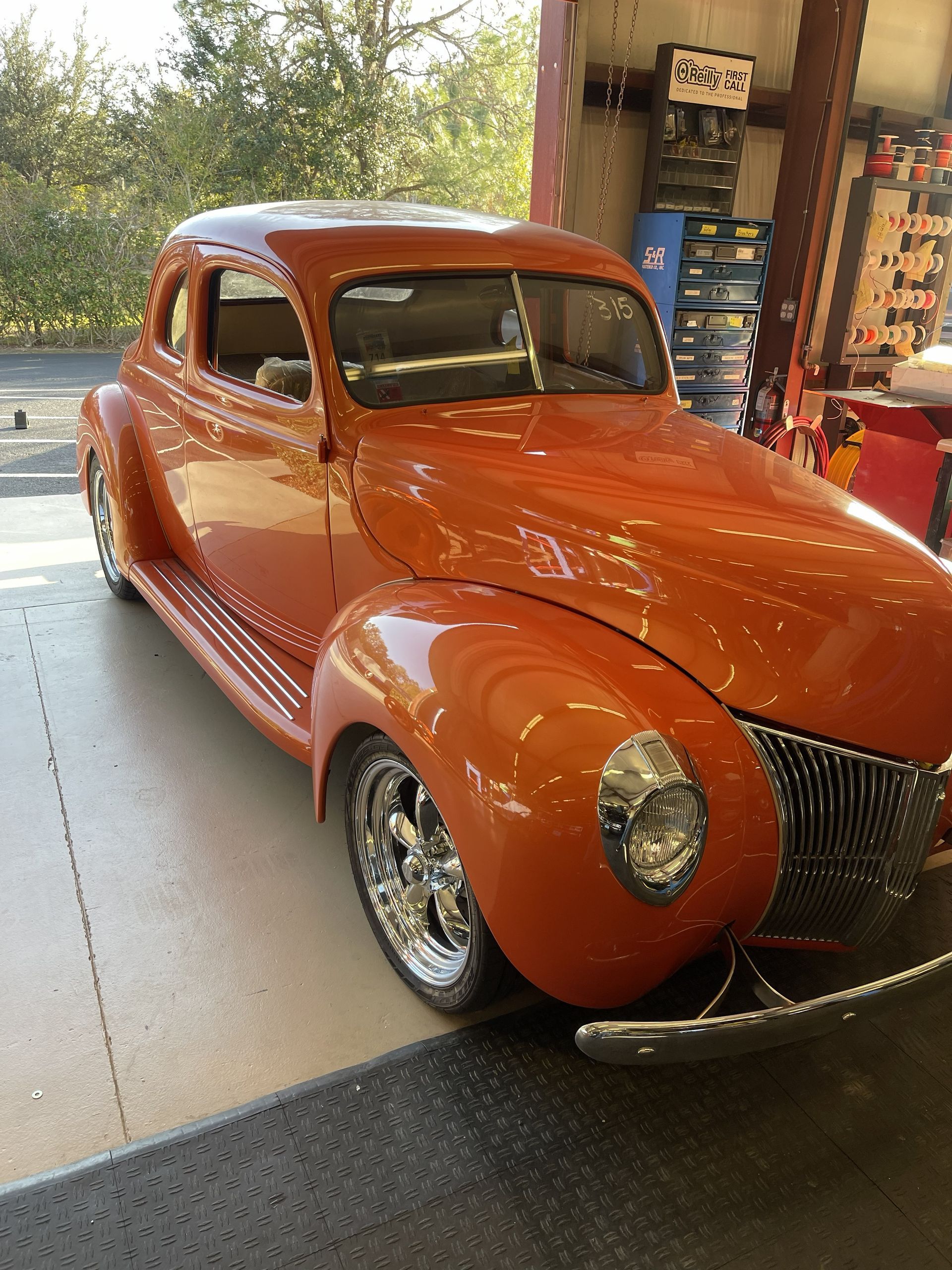 A restored, bright orange 1940s-style classic coupe with chrome wheels parked inside a garage.