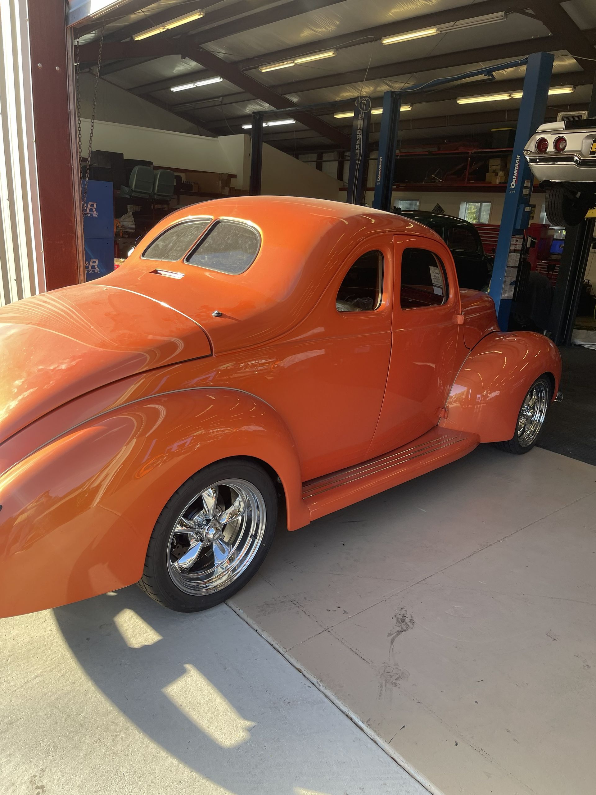 A bright orange vintage hot rod coupe parked inside a garage workshop.