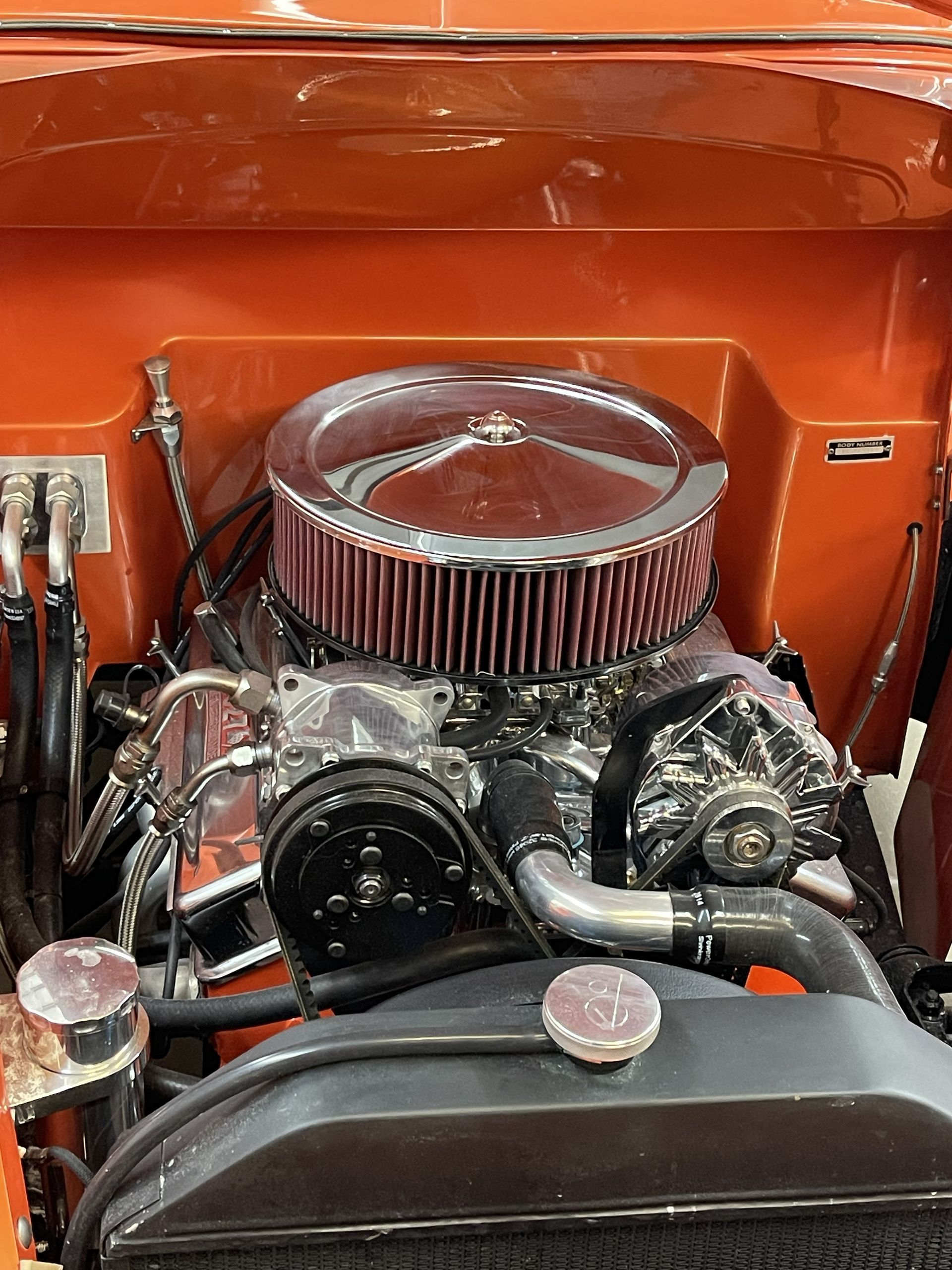 The clean engine bay of a classic vehicle, featuring a prominent chrome air cleaner set against vibrant orange paint.