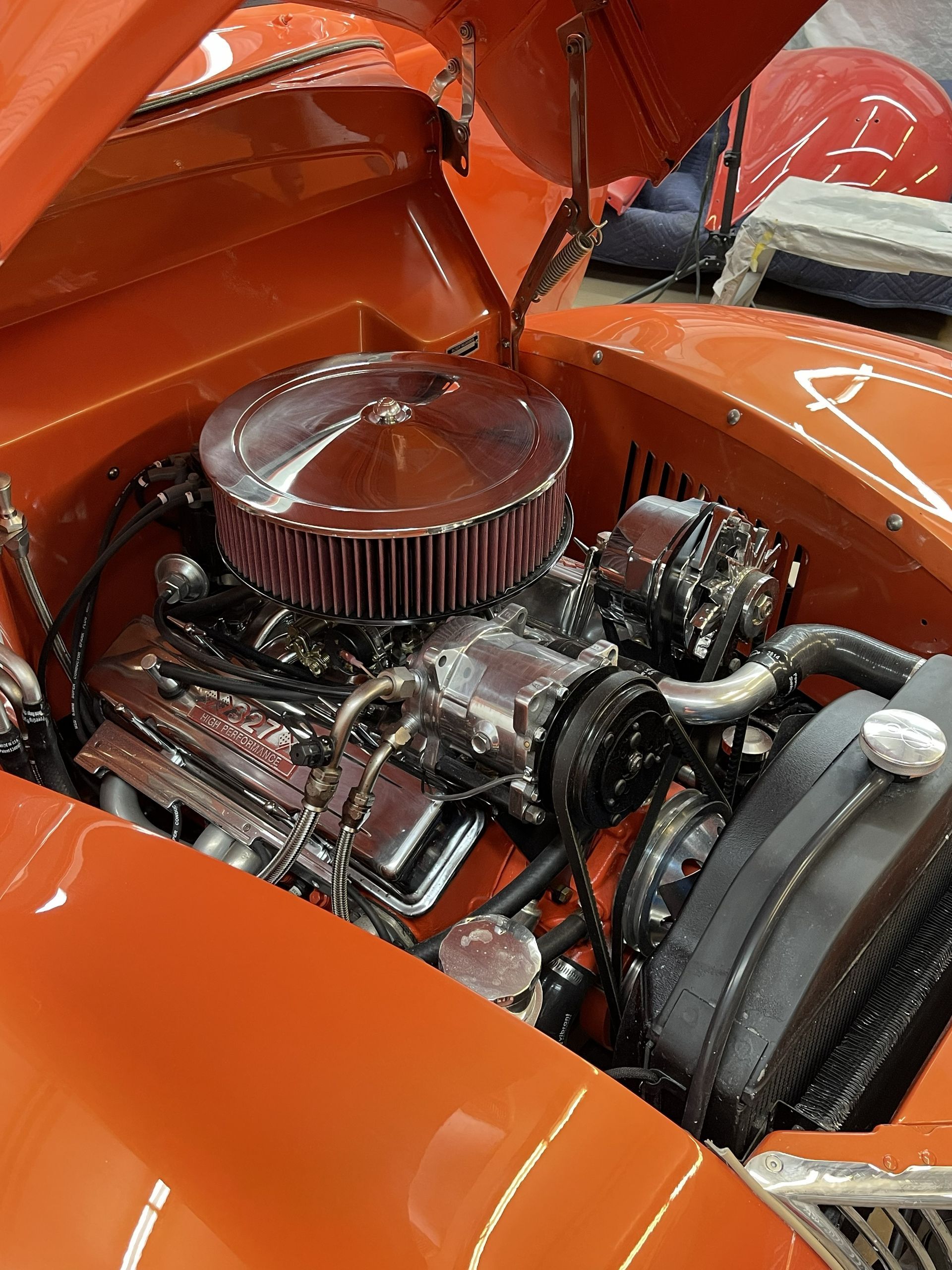 Shiny, chrome-topped V8 engine inside the open hood of a bright orange vintage car.