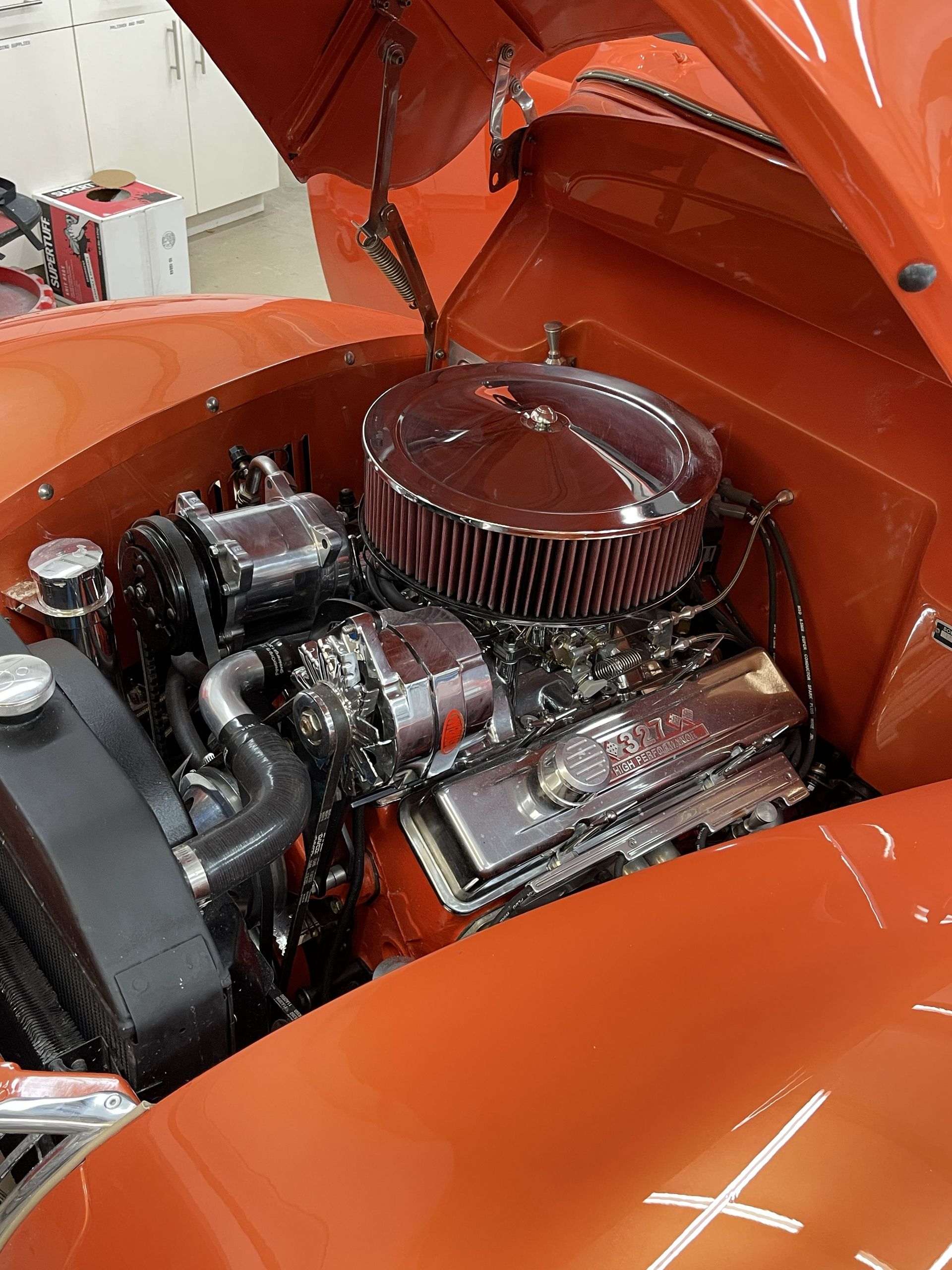 A clean engine bay of a classic orange car, featuring a large chrome air cleaner and polished engine components.
