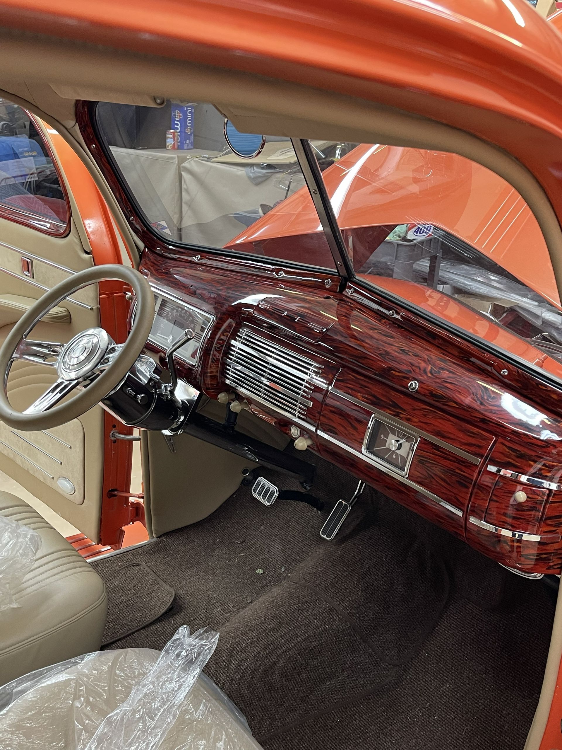 The interior of a classic car featuring a dark, wood-grain patterned dashboard, tan upholstery, and a chrome steering wheel.