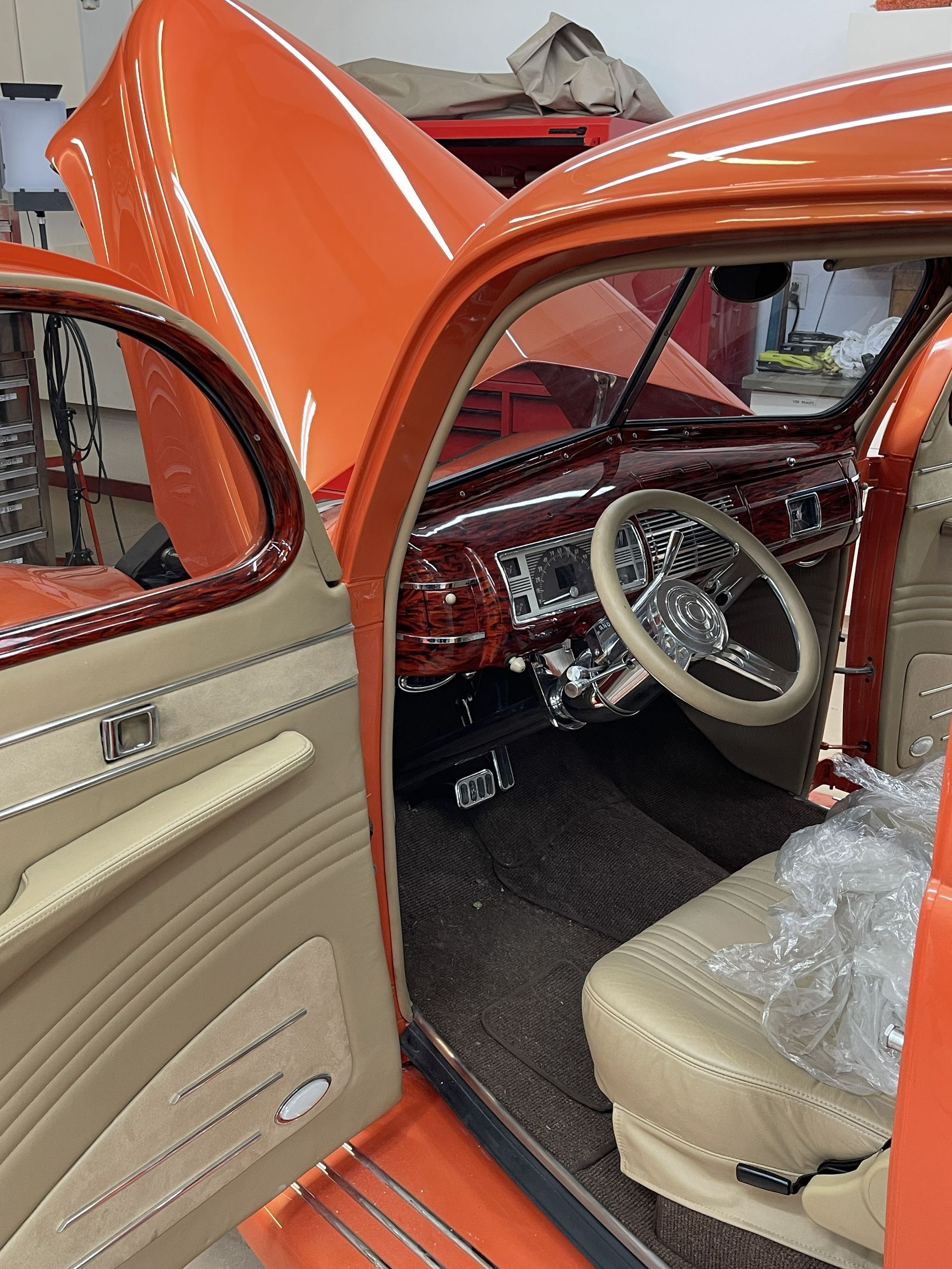 The interior of a vintage car with bright orange exterior paint, tan leather seats, and a metallic dashboard.
