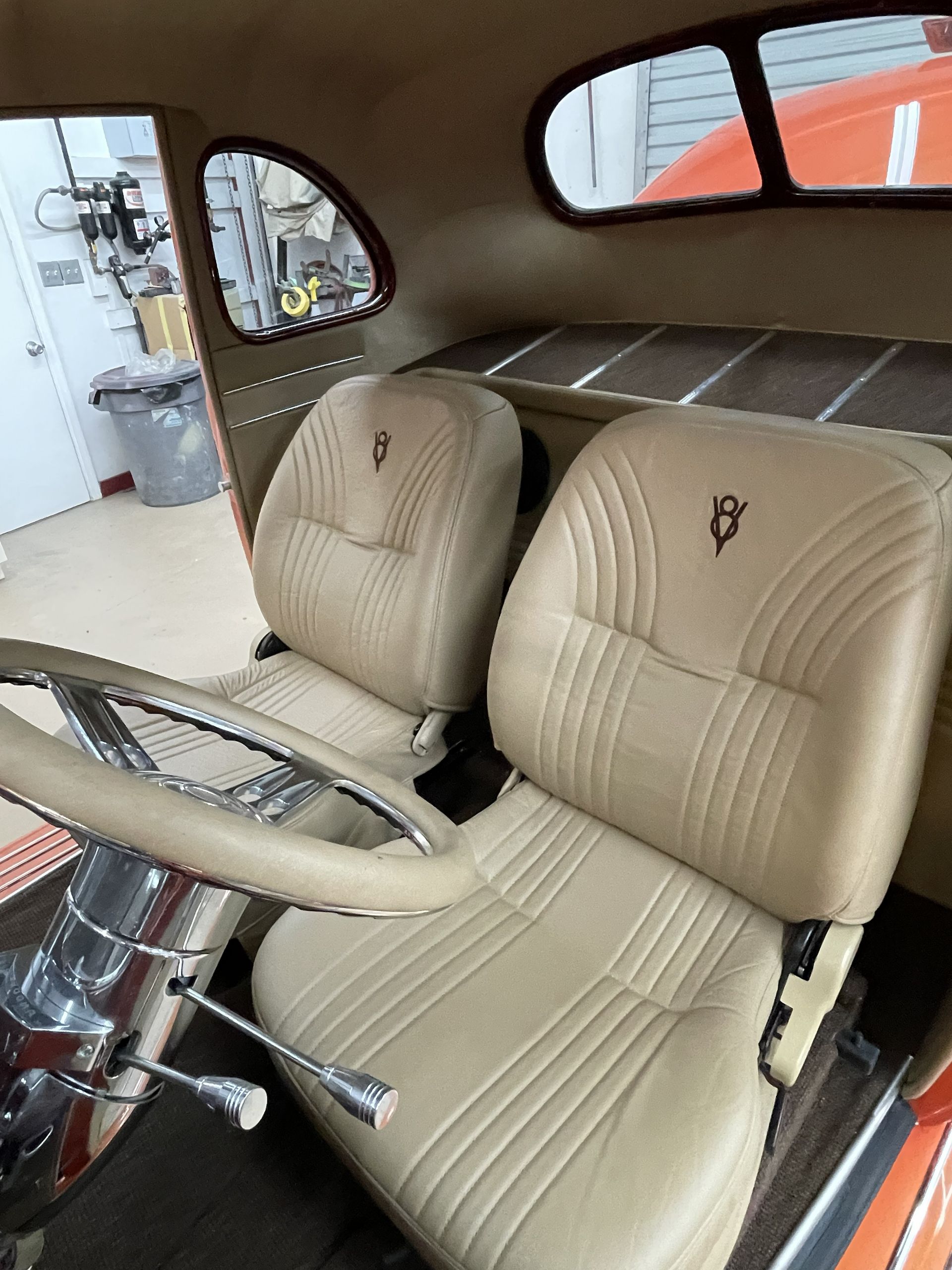 Interior view of a classic car with tan leather bucket seats, chrome steering column, and a wood-slat rear storage deck.