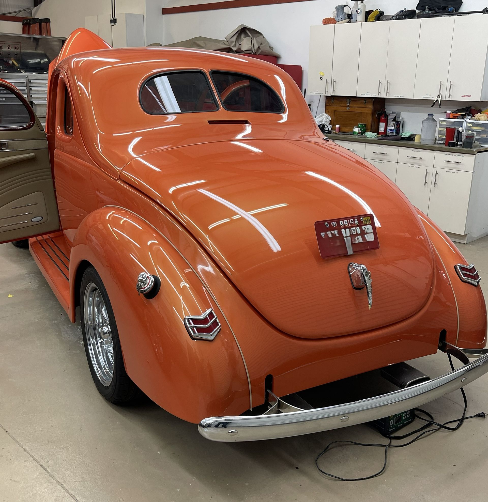 A bright orange vintage coupe parked inside a garage with its driver-side door open.