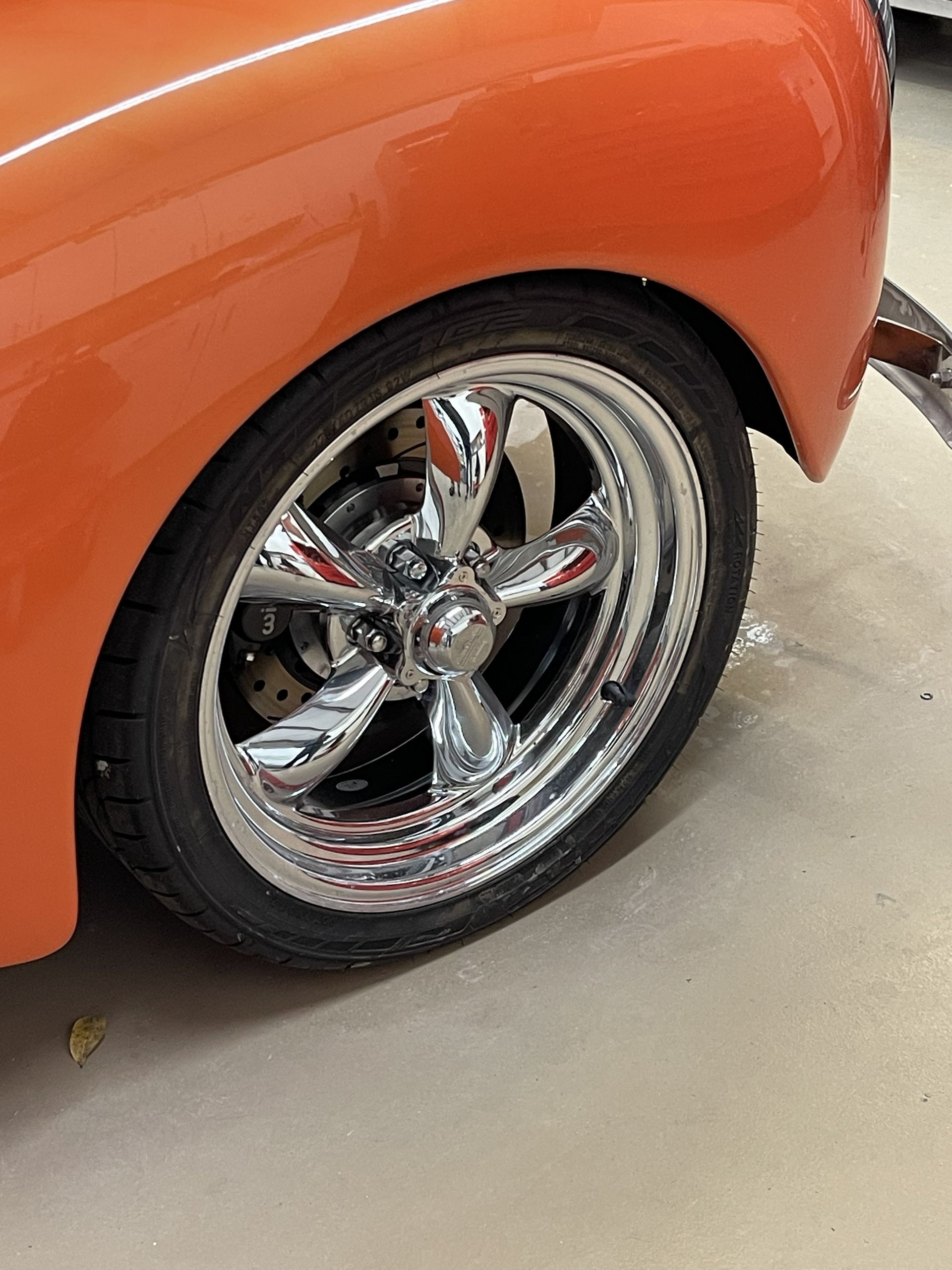 A close-up view of an orange car fender and a shiny chrome five-spoke wheel with a low-profile tire.