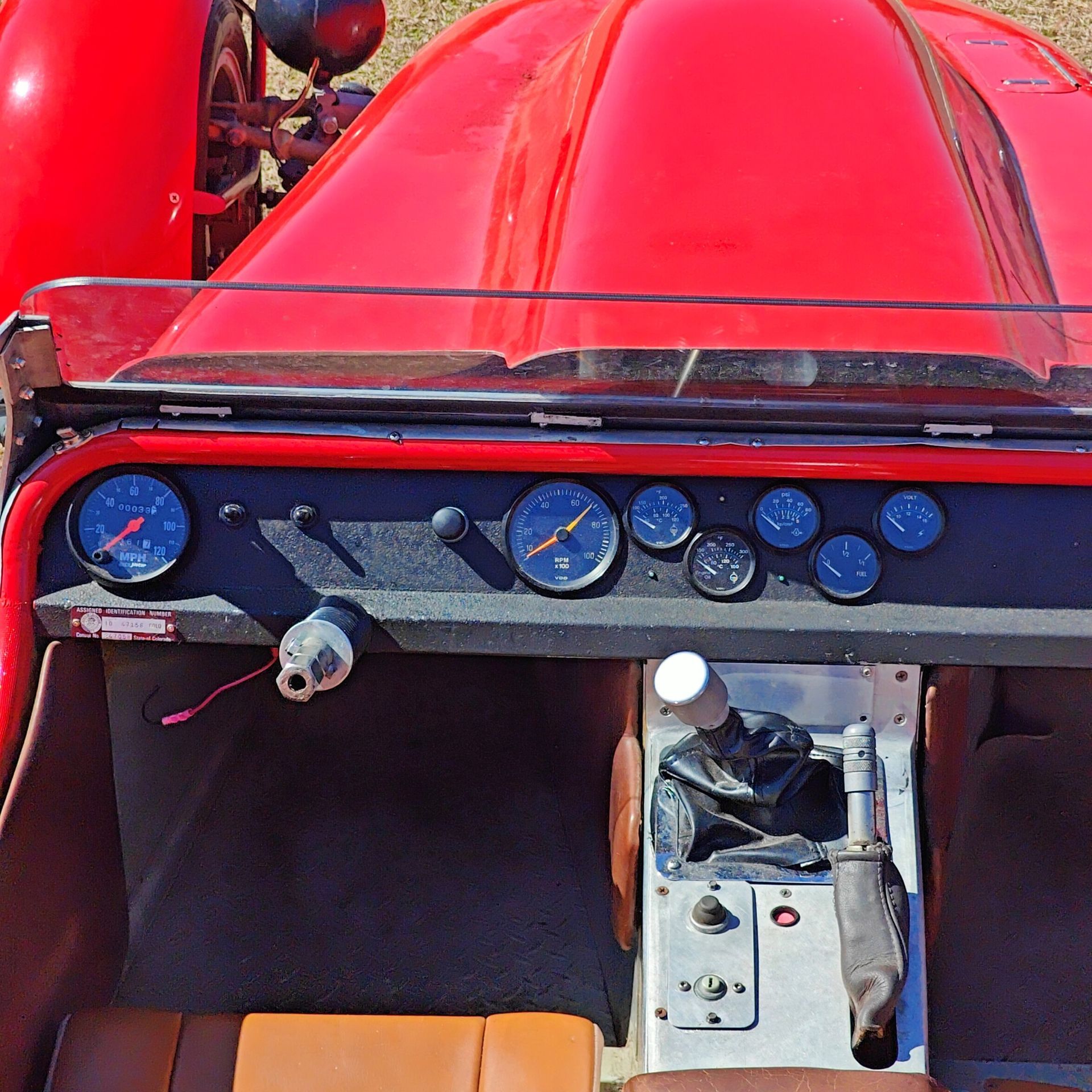 Interior view of a vintage red open-top car, featuring a black dashboard with round gauges and a manual gear shifter.