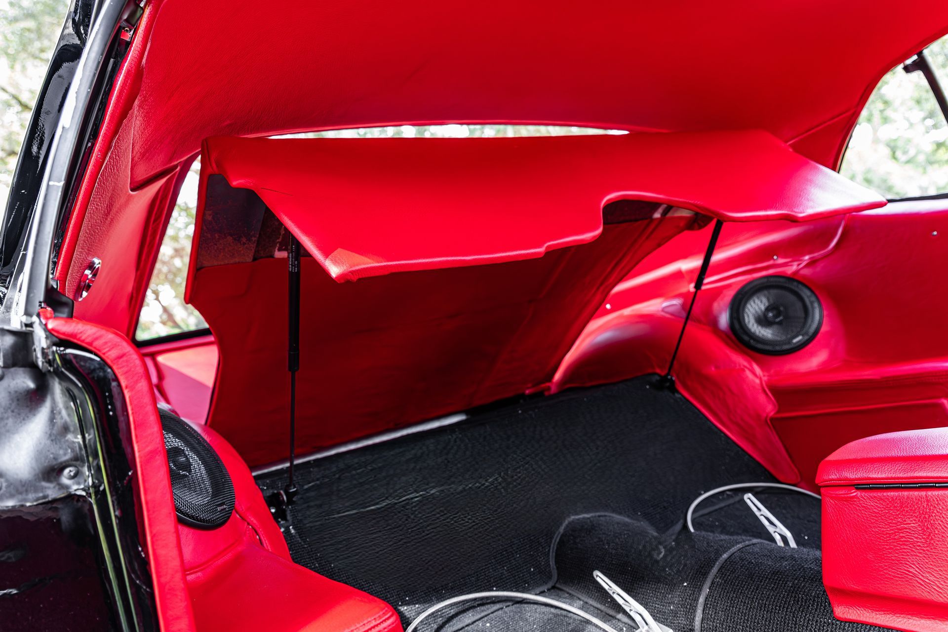 The interior of a vehicle trunk is lined with vibrant red upholstery and black carpeting, featuring two speakers.