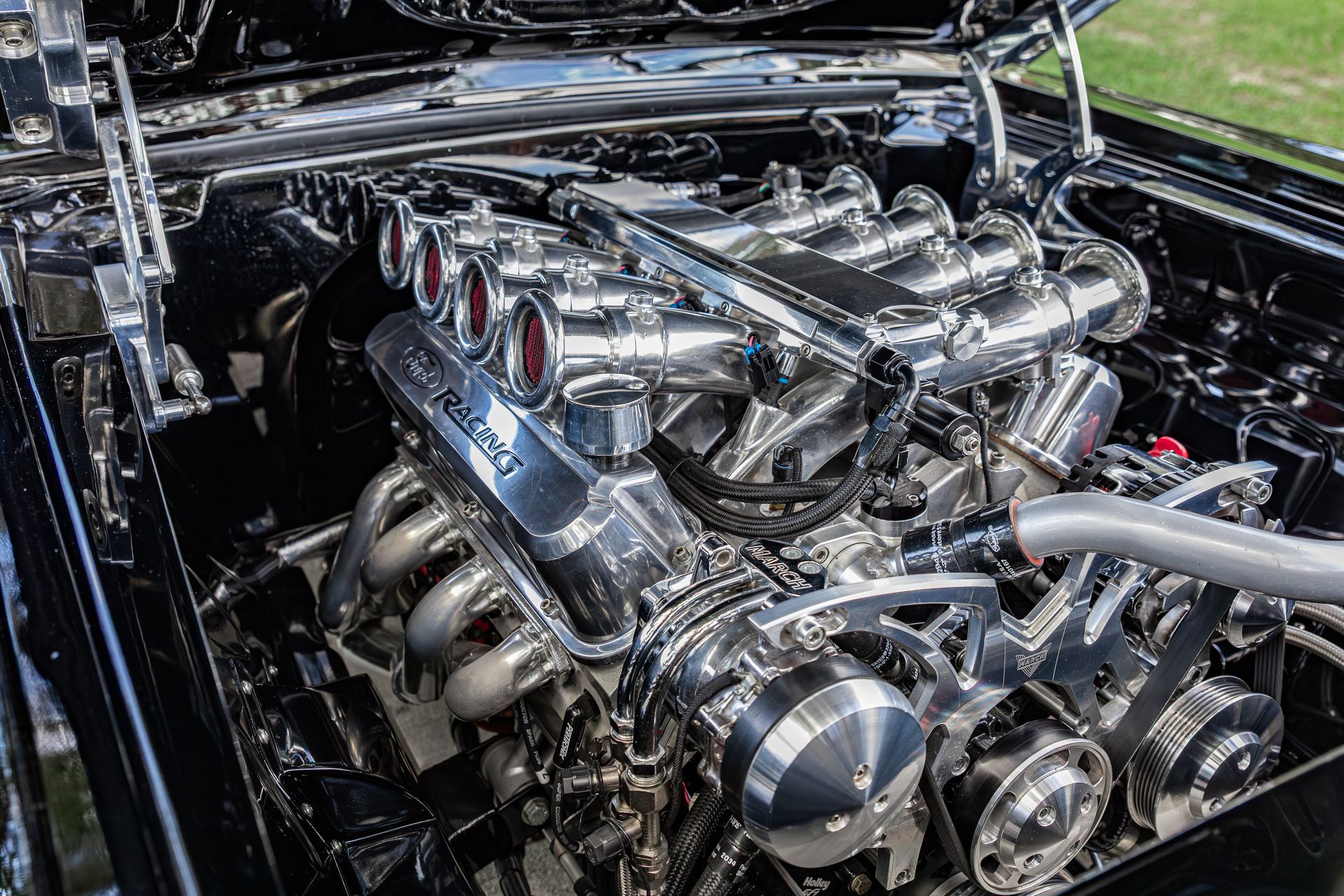 A highly polished, chrome-plated V8 car engine under an open hood, reflecting light with intricate mechanical detail.