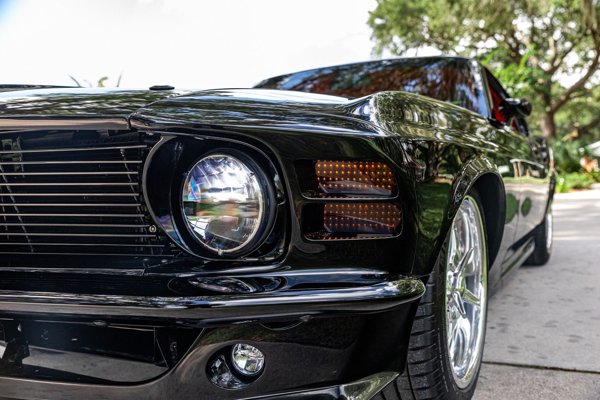 Close-up, low-angle shot of a shiny black 1970 Ford Mustang’s front end, highlighting its circular headlight and alloy wheel.