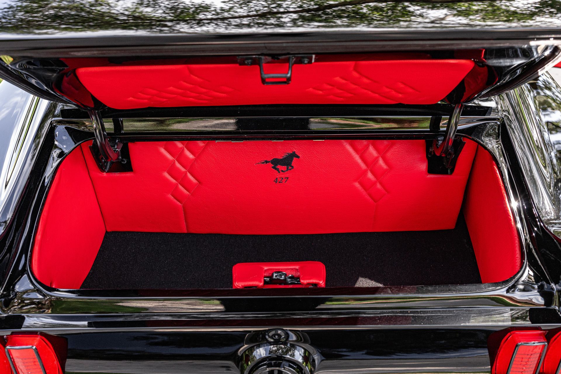 Open trunk of a black Ford Mustang featuring bright red quilted interior lining and a Mustang pony emblem.
