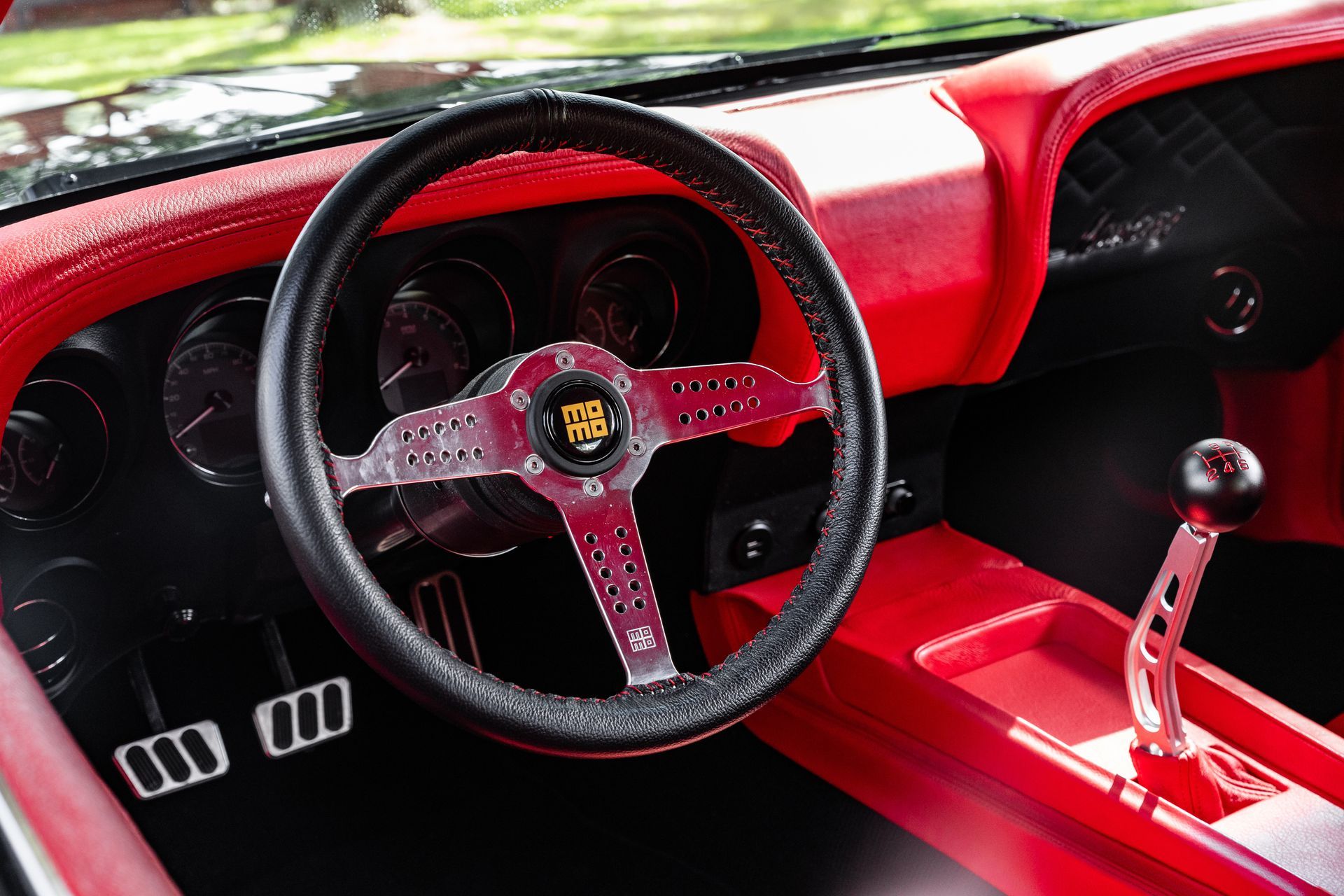 The interior of a classic car featuring a red dashboard, a black leather steering wheel, and a metal gear shifter.