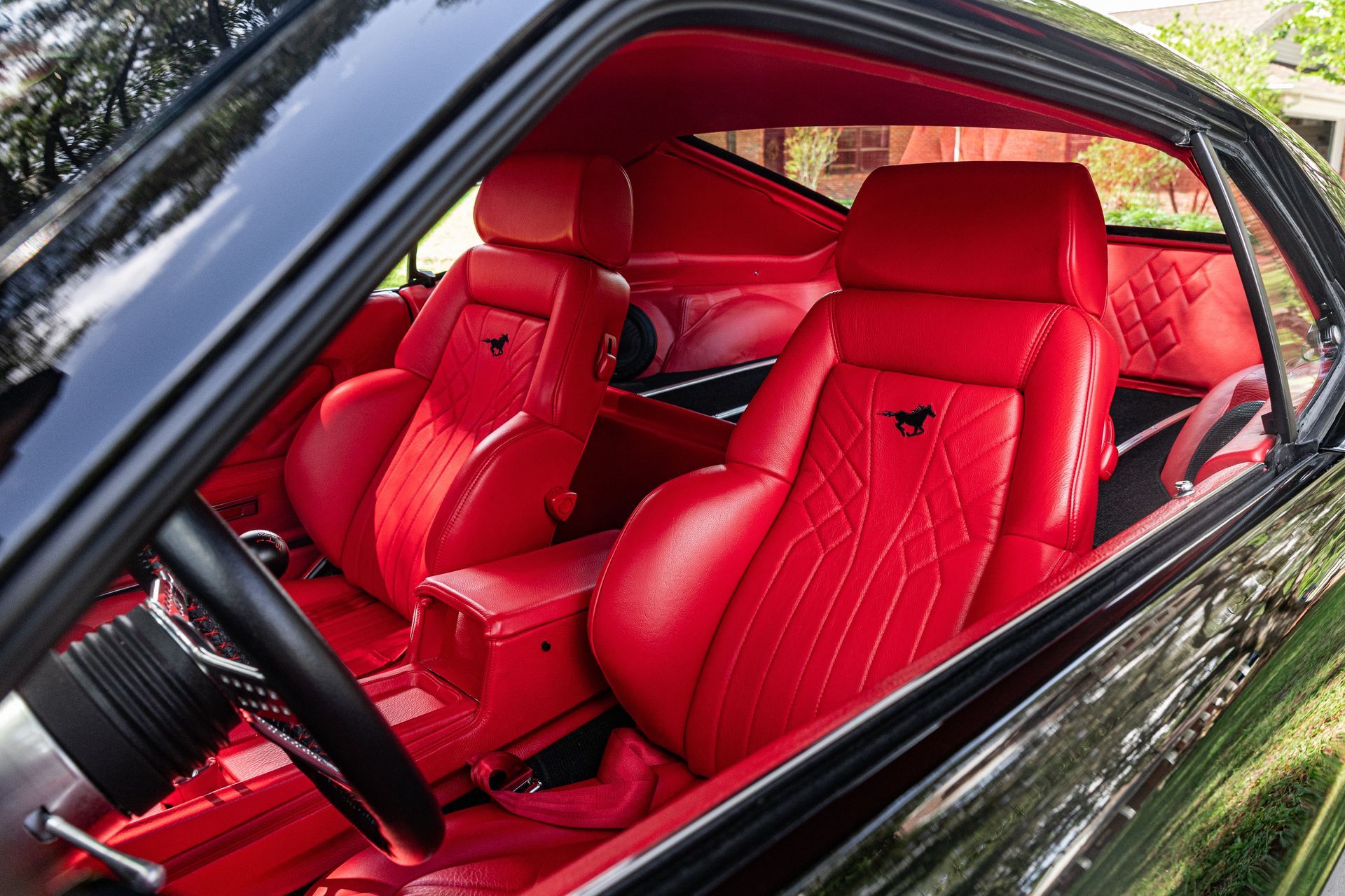 A black car's interior featuring vibrant red, custom-quilted leather bucket seats with the Mustang logo.