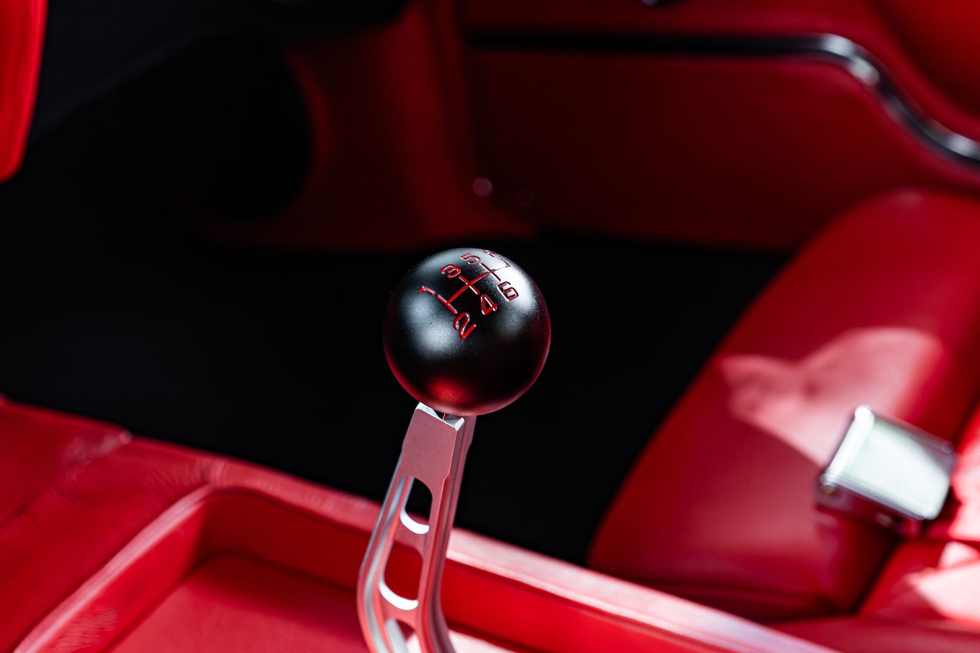 Close-up of a black manual gear shift knob with a red gear pattern, set against a vibrant red car interior.