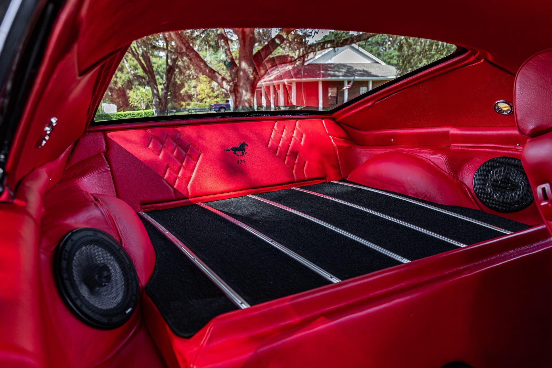 The interior of a red car featuring a folded back seat, black floor matting with silver trim, and side-mounted speakers.