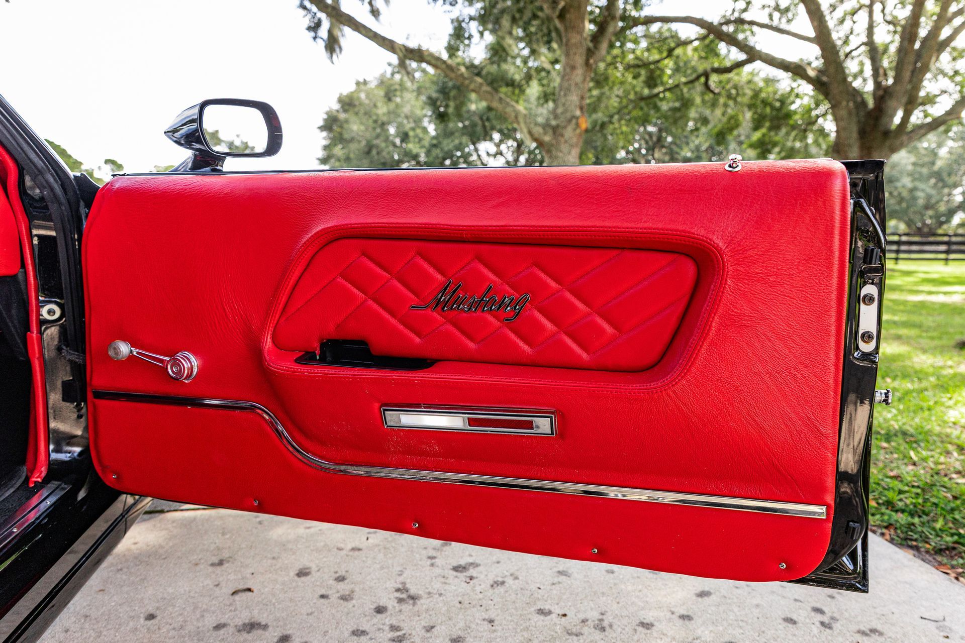 A bright red, quilted car door panel with a chrome handle and manual crank window, set against a blurry outdoor background.