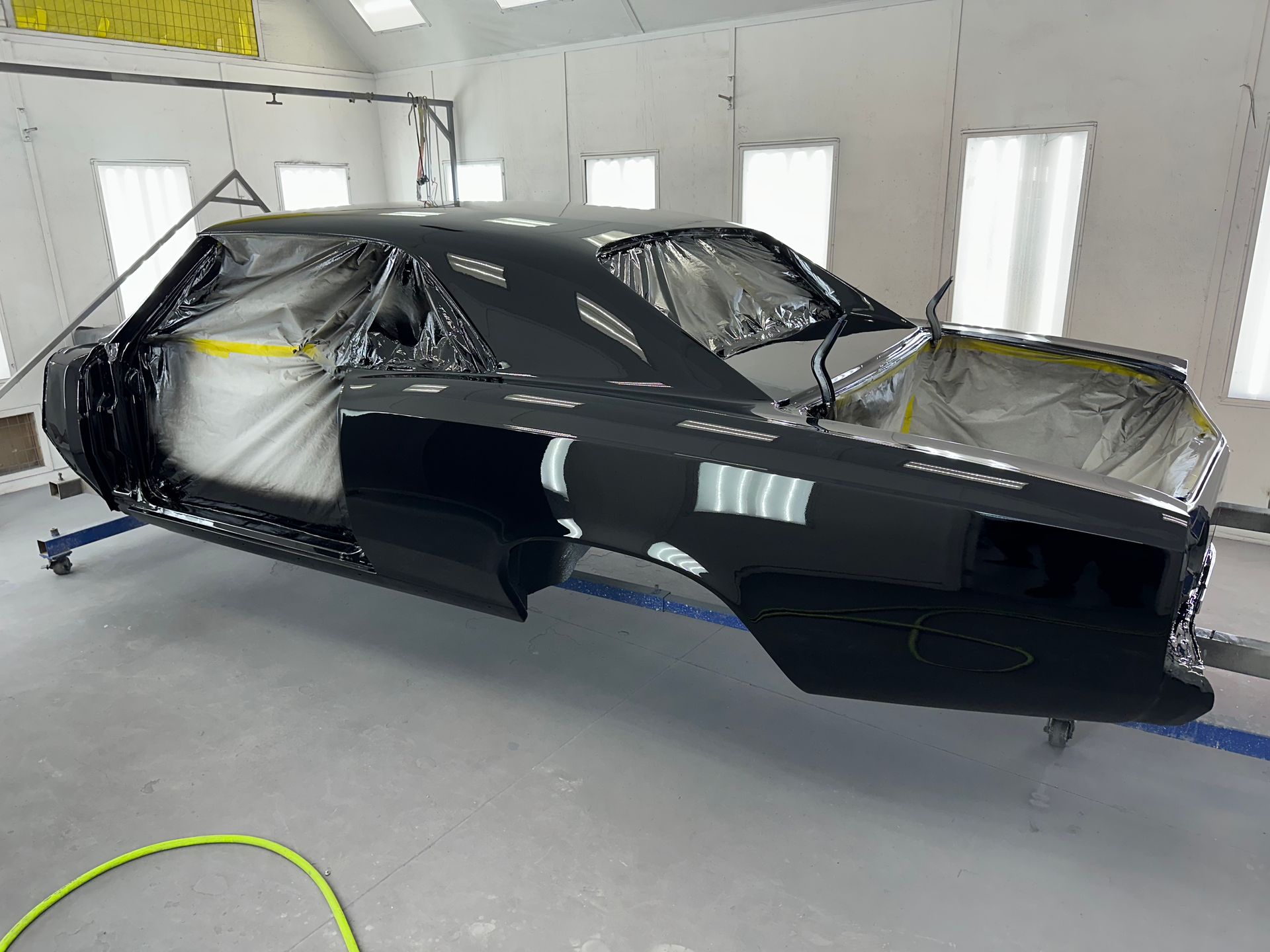 A black muscle car body undergoing paint and restoration in a brightly lit professional garage.