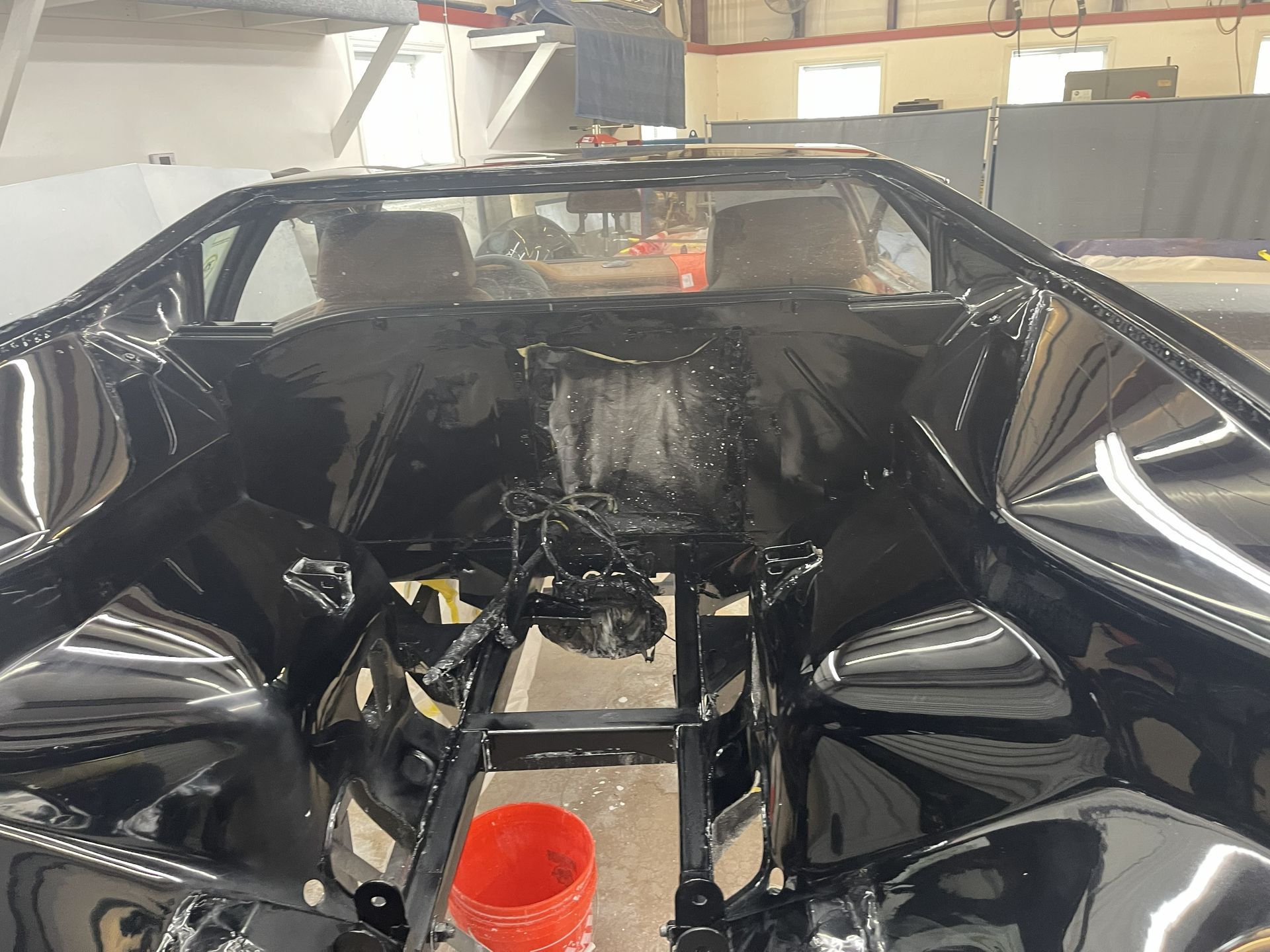 A stripped-down, high-gloss black car chassis inside a workshop, with a bright orange bucket on the floor.