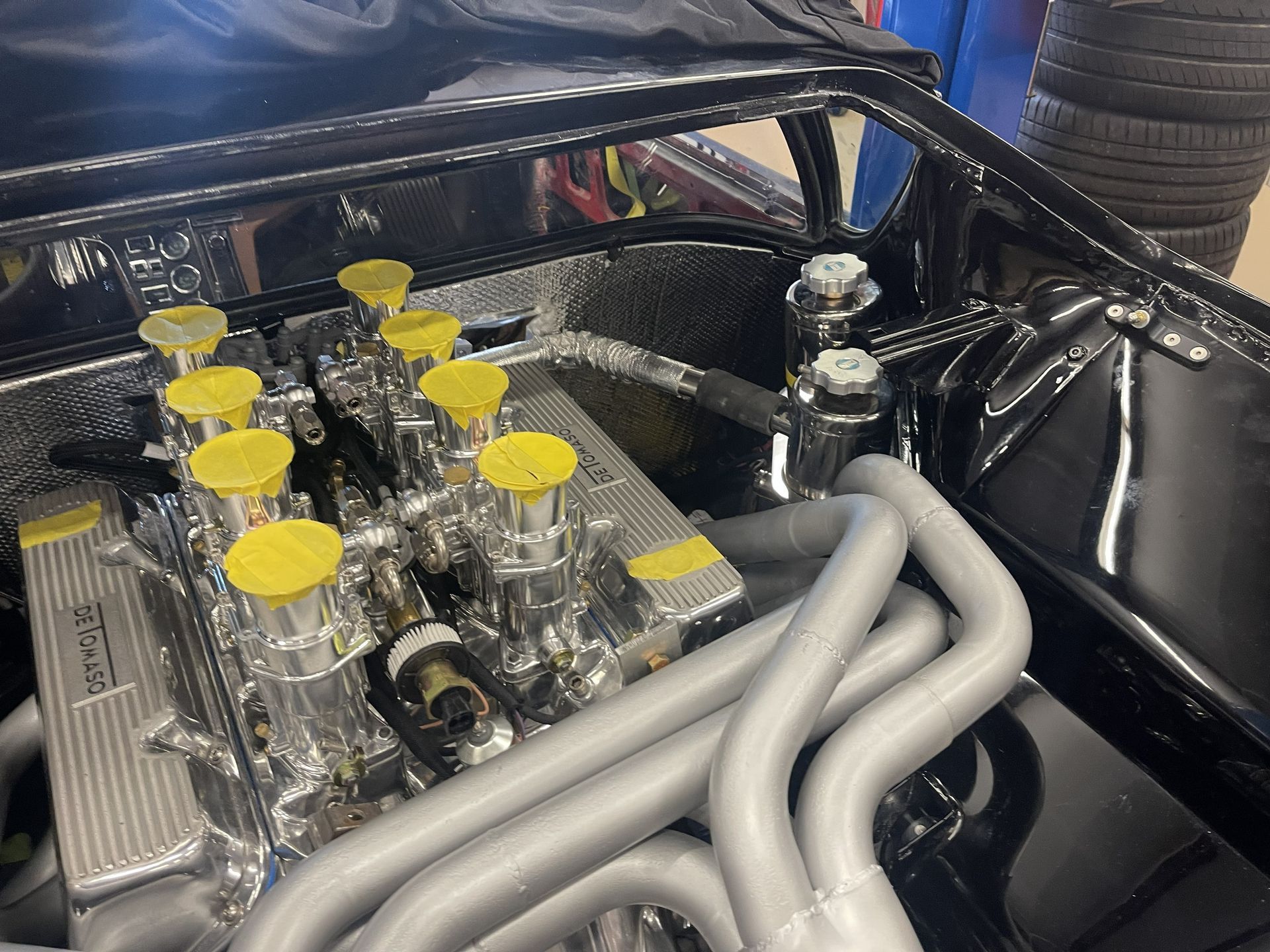 A close-up of a high-performance car engine with silver components and bright yellow intake covers in a black engine bay.