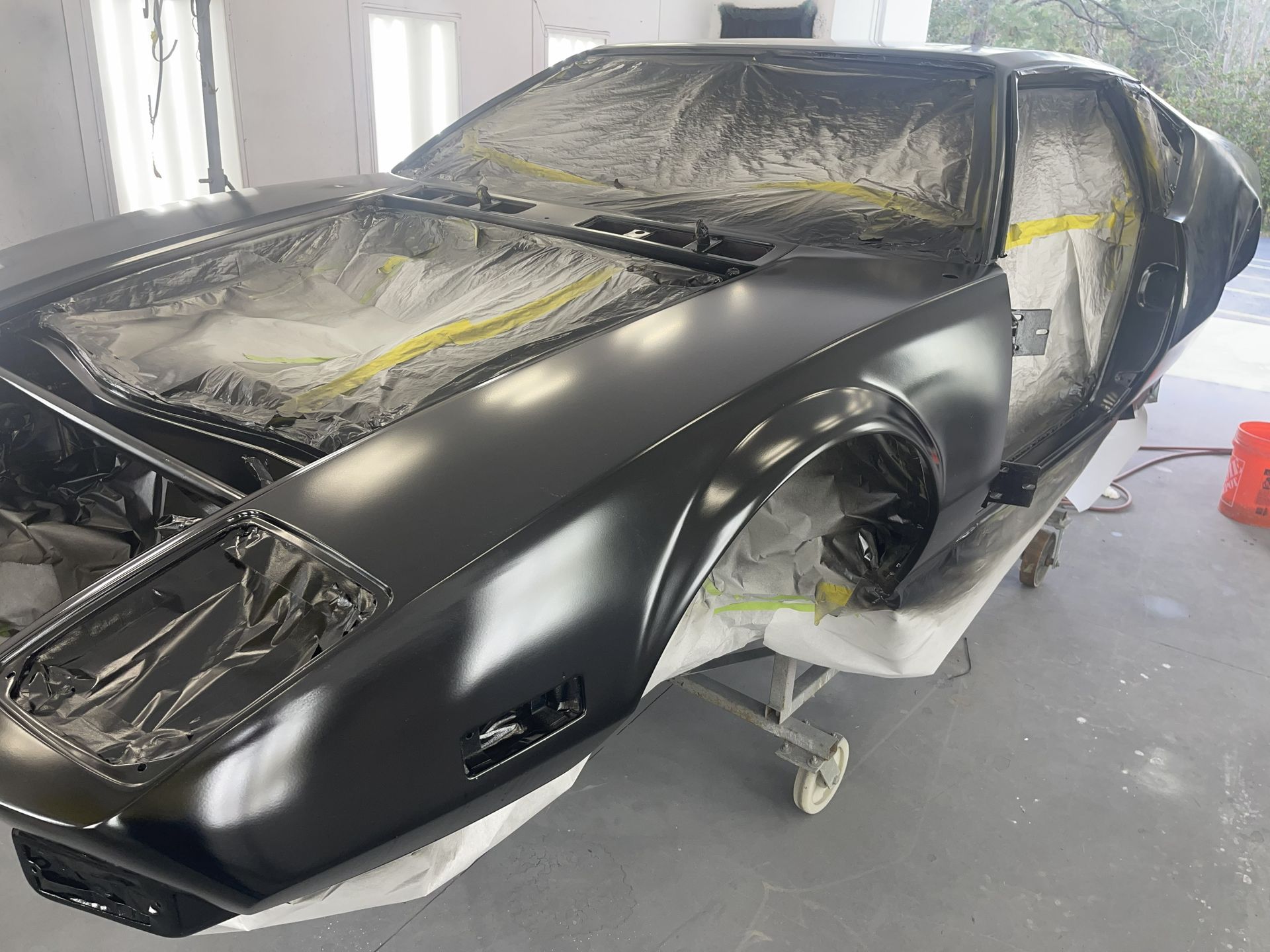 A black De Tomaso Pantera in a body shop, masked for paint with protective plastic over its windows and hood.