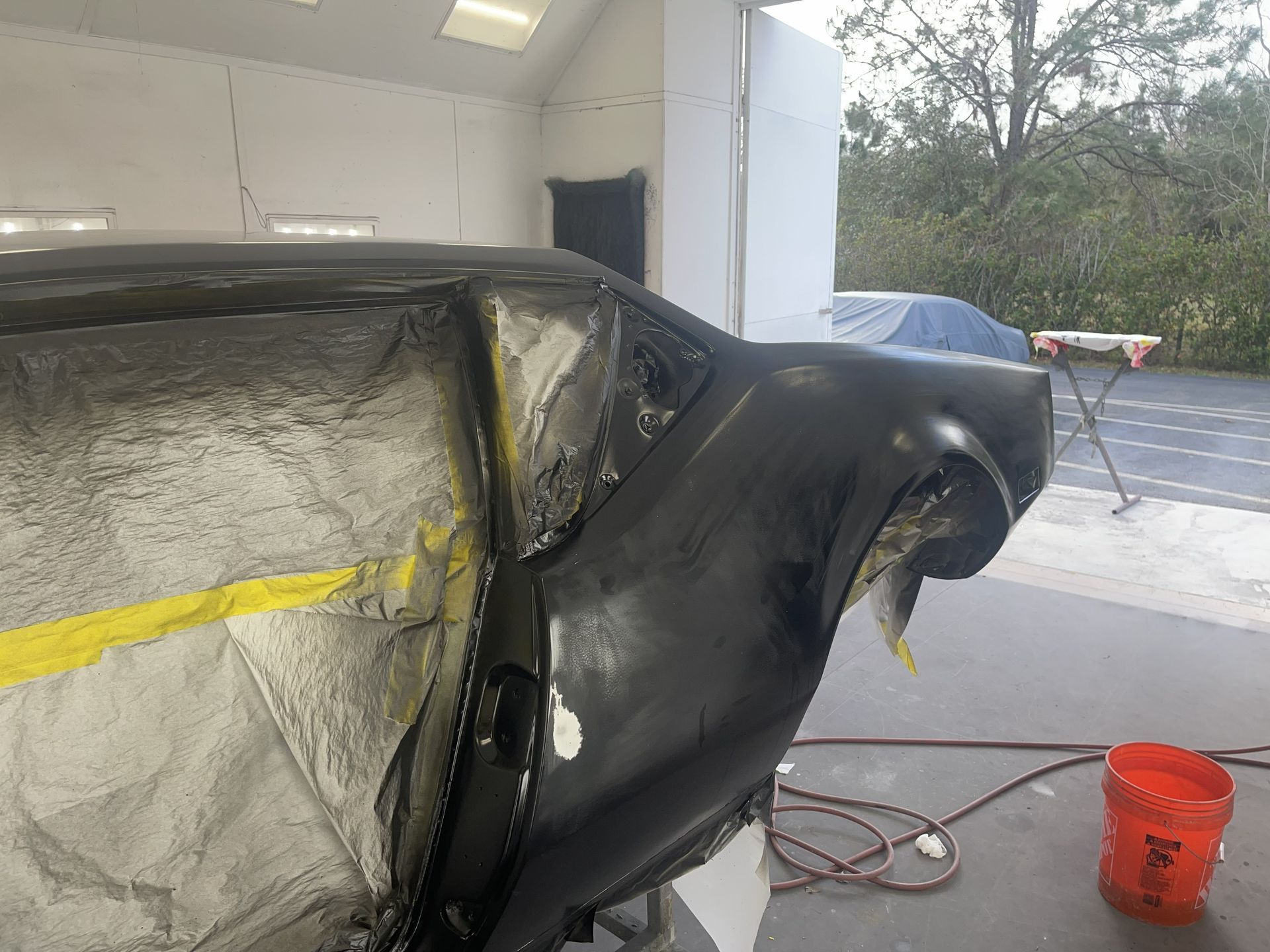 A car chassis in a workshop, masked with tape and protective film, undergoing body work in a garage setting.