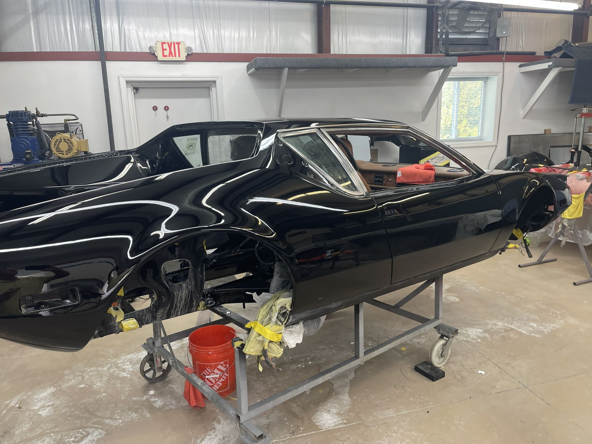 A black sports car body frame sits on a metal stand inside an automotive workshop.