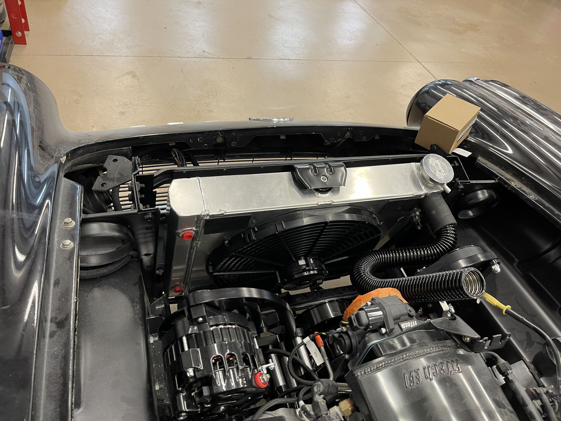 A high-angle view of a car engine bay featuring a polished aluminum radiator, black cooling fan, and alternator.