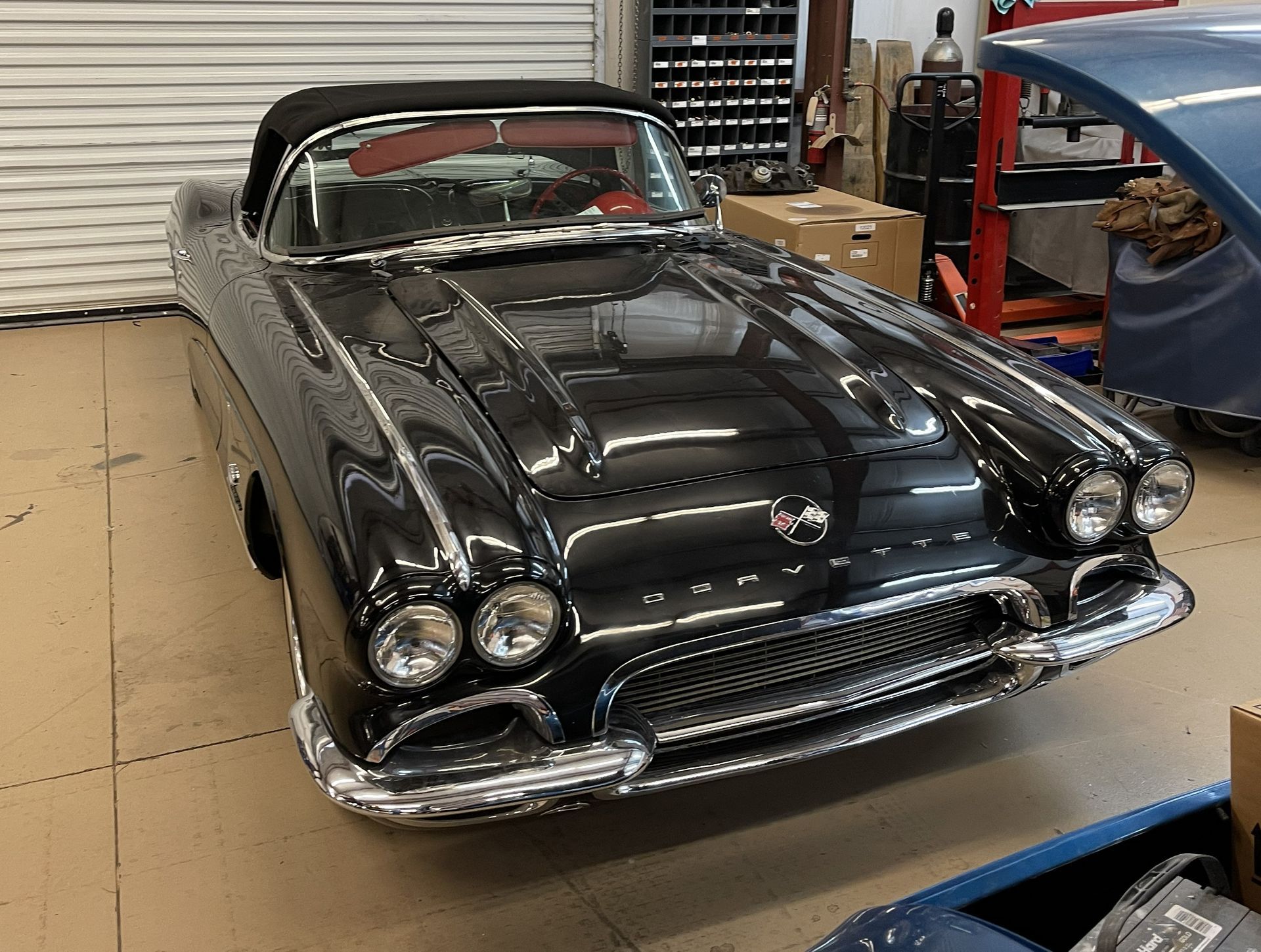 A black 1958 Chevrolet Corvette convertible parked inside a garage workshop.