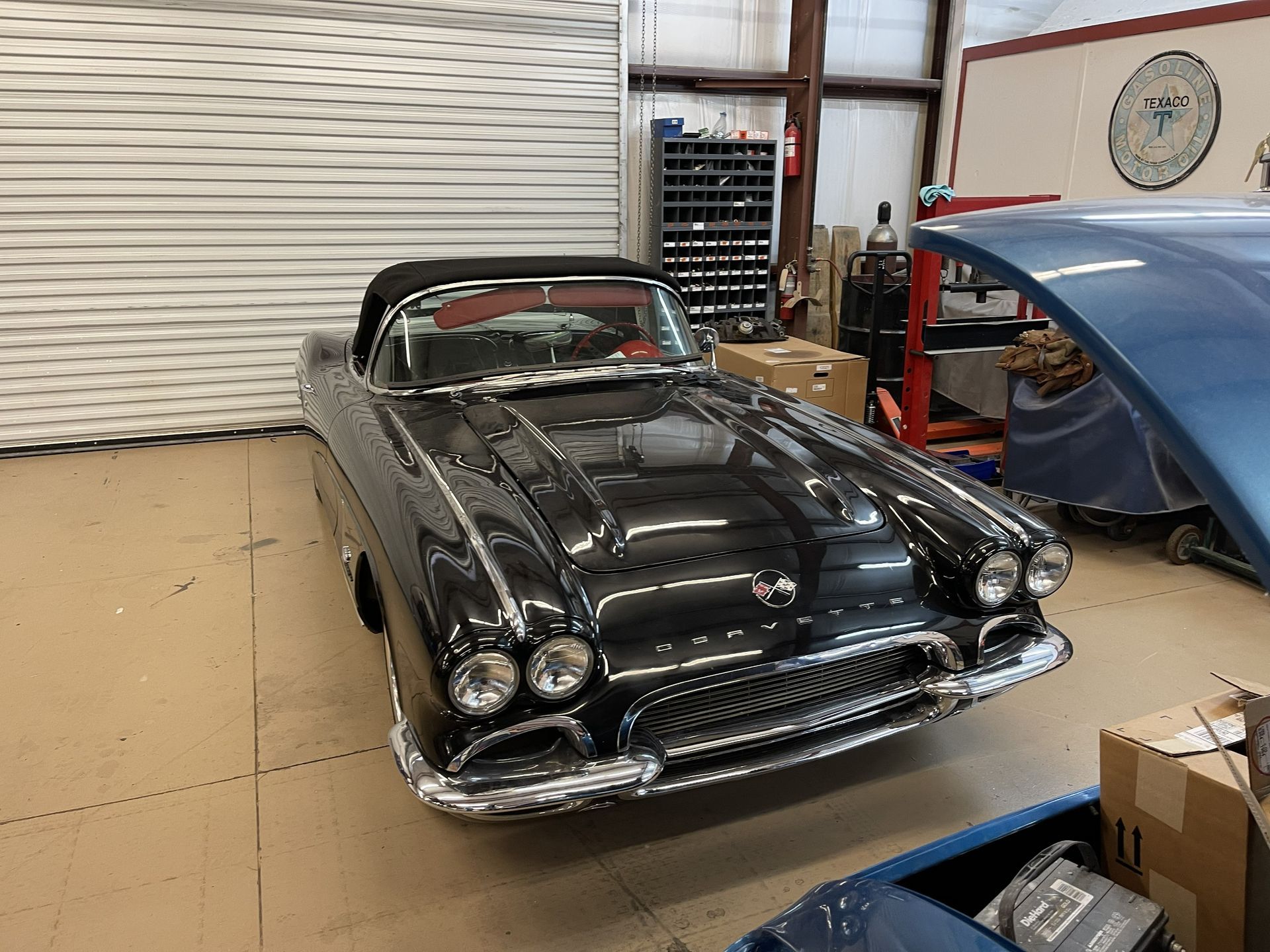 A dark, restored classic convertible sports car parked inside a garage workshop.