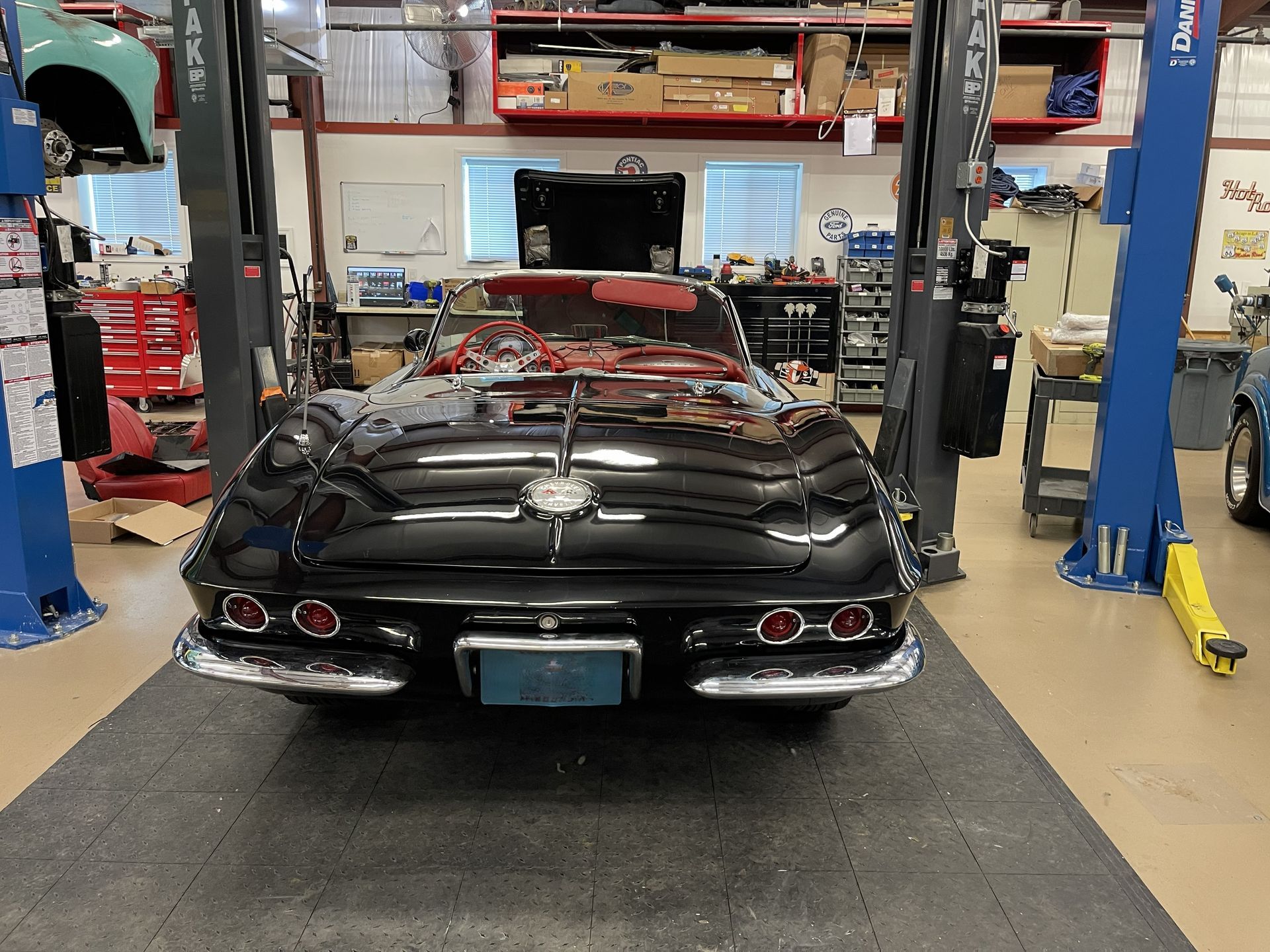 A black vintage Chevrolet Corvette parked inside a mechanic's garage between two blue car lifts.