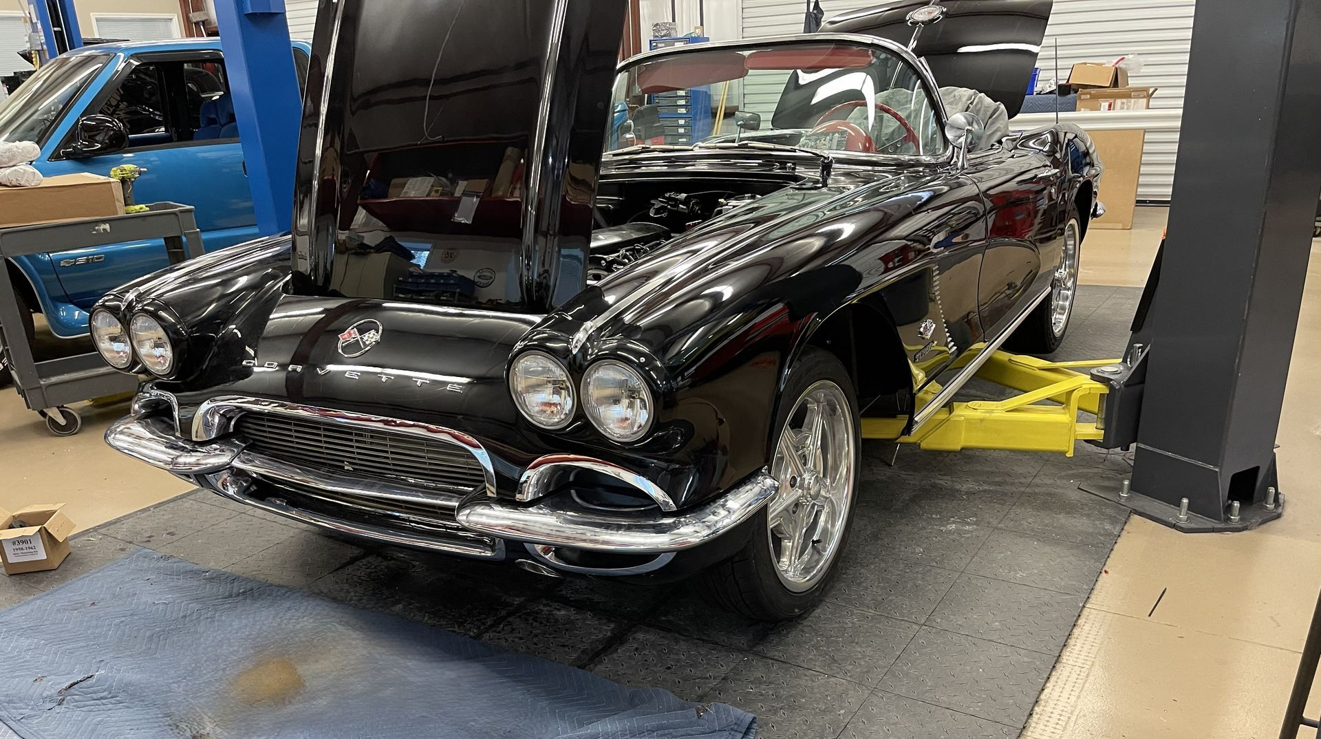 A black classic Chevrolet Corvette convertible with its hood open in an auto repair shop.