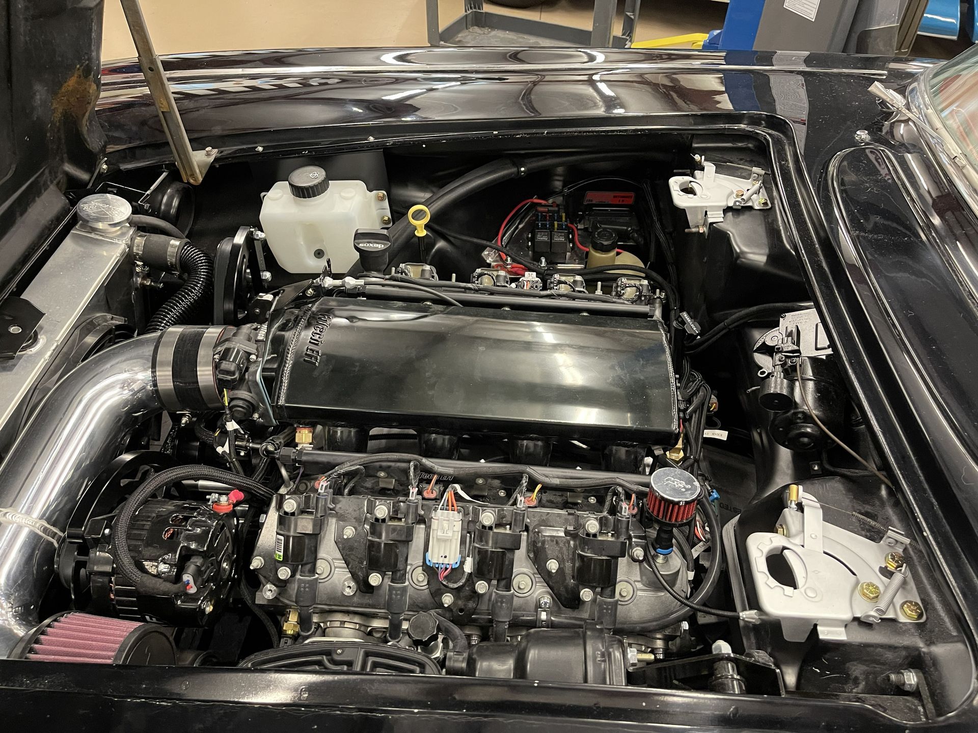Engine bay of a black classic car featuring a modern, high-performance V8 engine with a black intake manifold.