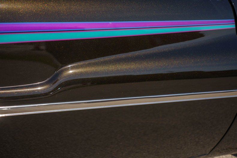 Close-up of a metallic black car door featuring a horizontal design stripe in shades of purple and teal.