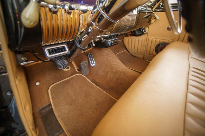 Interior of a vintage car with tan leather bench seating, brown carpet, and a chrome-accented dashboard.