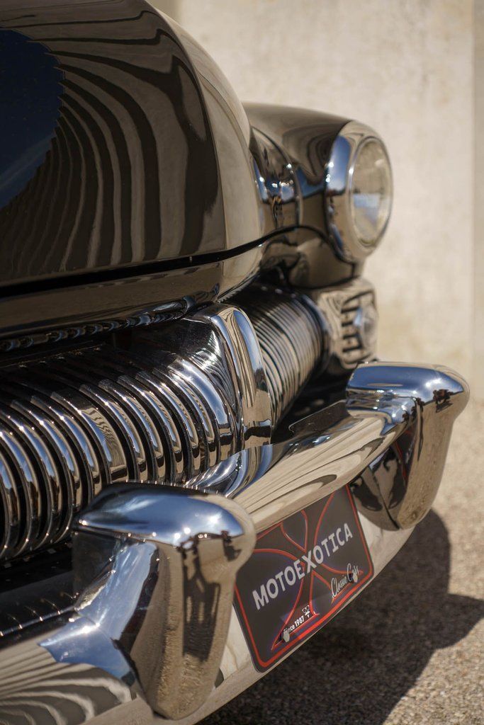 Close-up view of the shiny chrome grille, bumper, and headlight of a classic black vintage car.