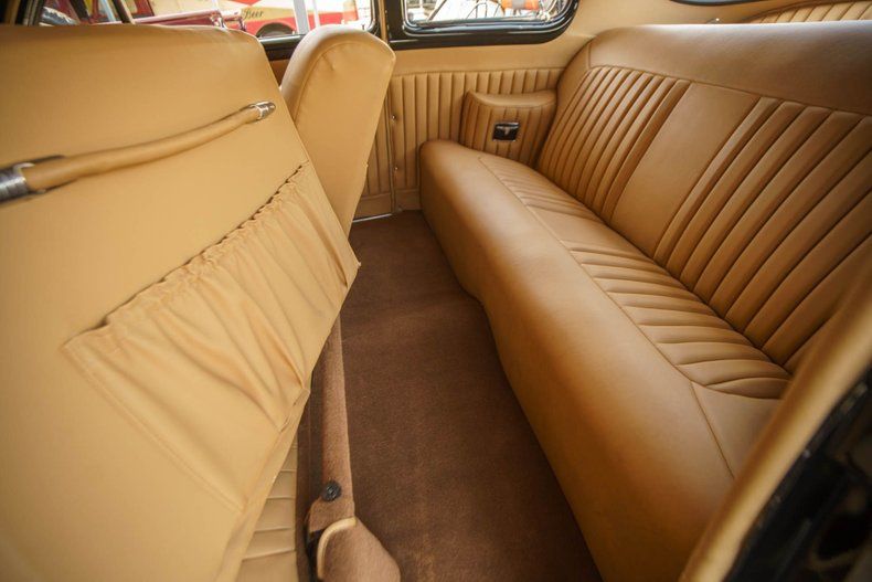 The tan leather interior of a vintage car, featuring a backseat and a pocketed front seat back.