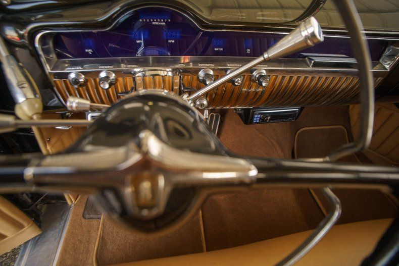 Interior view of a classic car dashboard with wood grain paneling, a large steering wheel, and a blue instrument cluster.