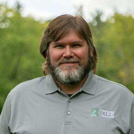 A man with a beard is wearing a grey shirt with the word life on it.