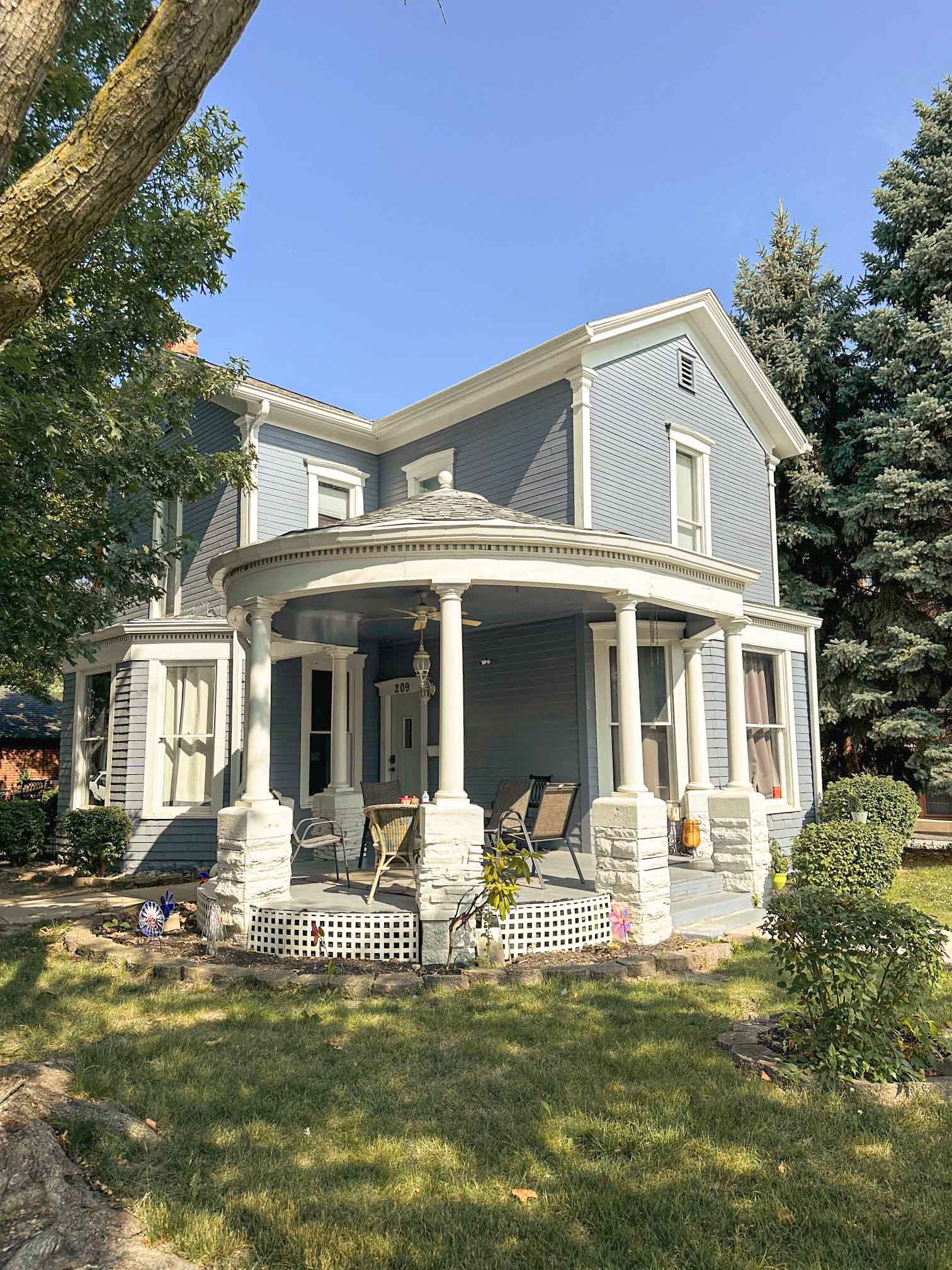 A large blue house with a porch and chairs in front of it.