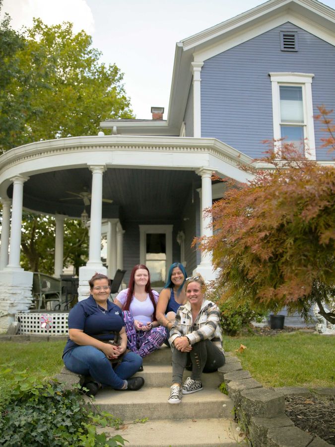 A group of women are sitting on the steps of a blue house.