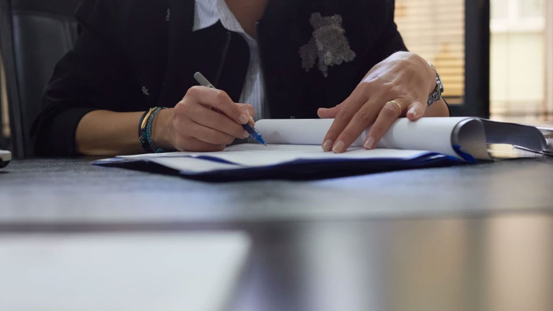 A woman is sitting at a desk writing on a piece of paper.