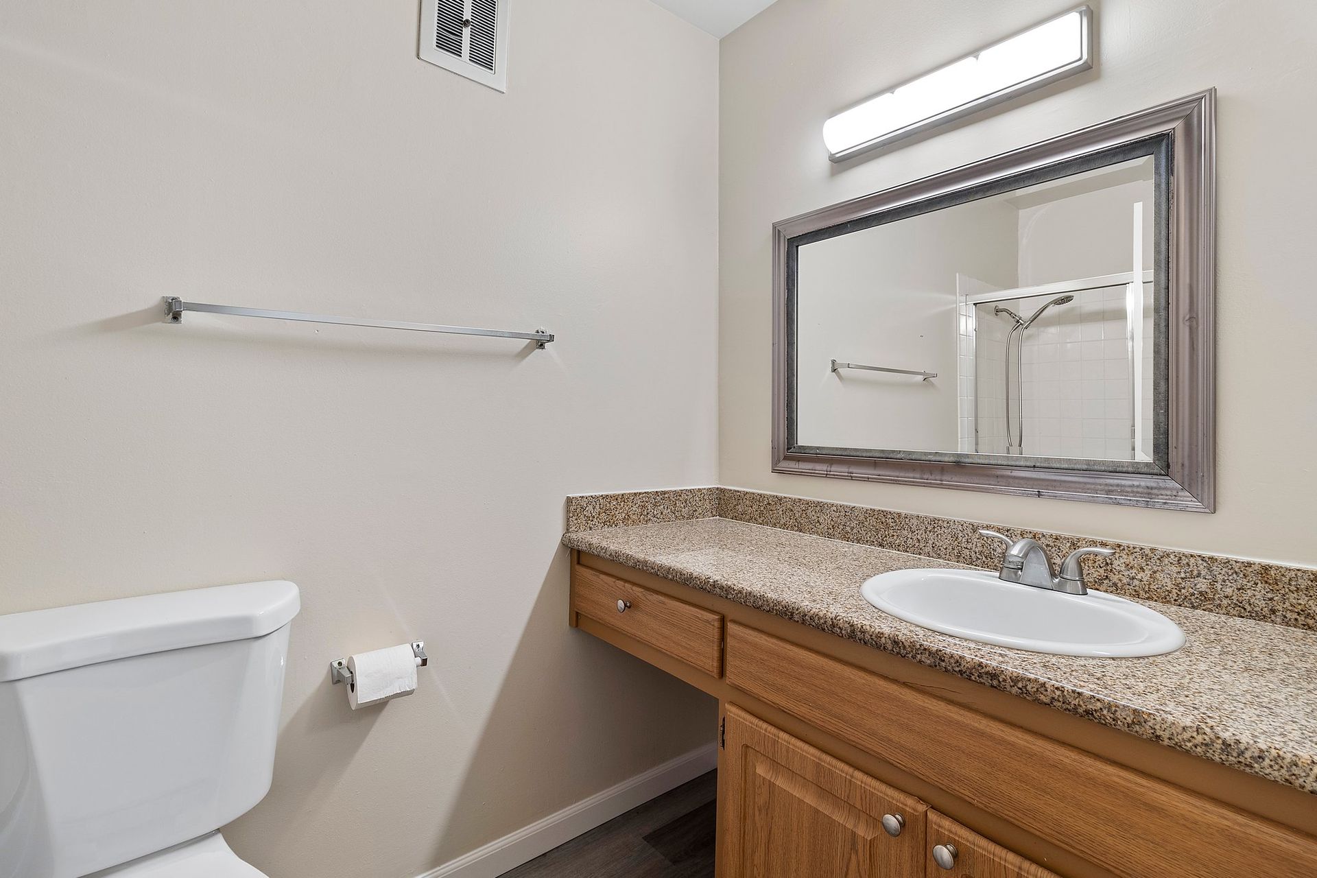 A bathroom with light walls, a wood vanity, granite-look countertop, oval sink, mirror with decorative frame, and toilet at Parkview Apartments.
